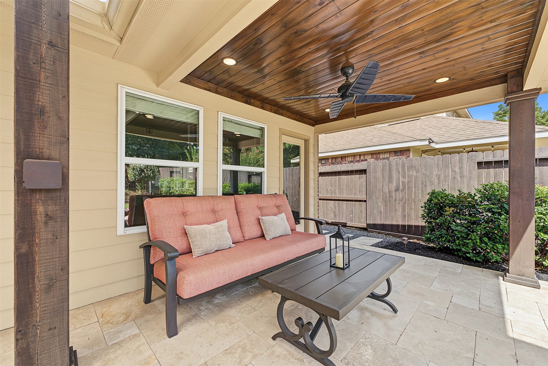 Charming covered patio with a cozy seating area, elegant stone flooring, and a stylish ceiling fan, perfect for outdoor relaxation.