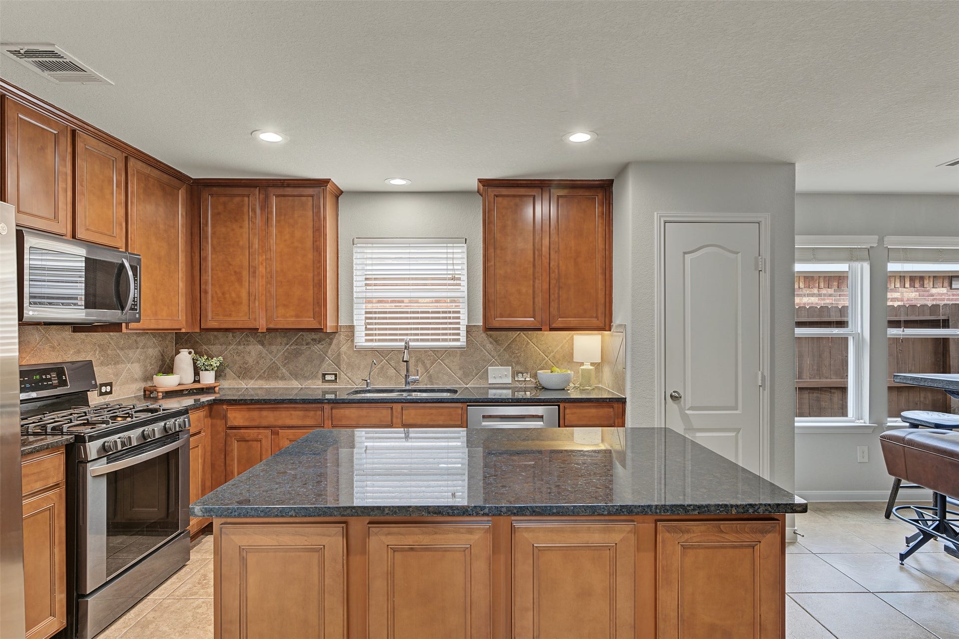 Modern kitchen featuring rich wood cabinetry, sleek granite countertops, and stainless steel appliances, accented by a central island for versatile cooking and dining experiences.