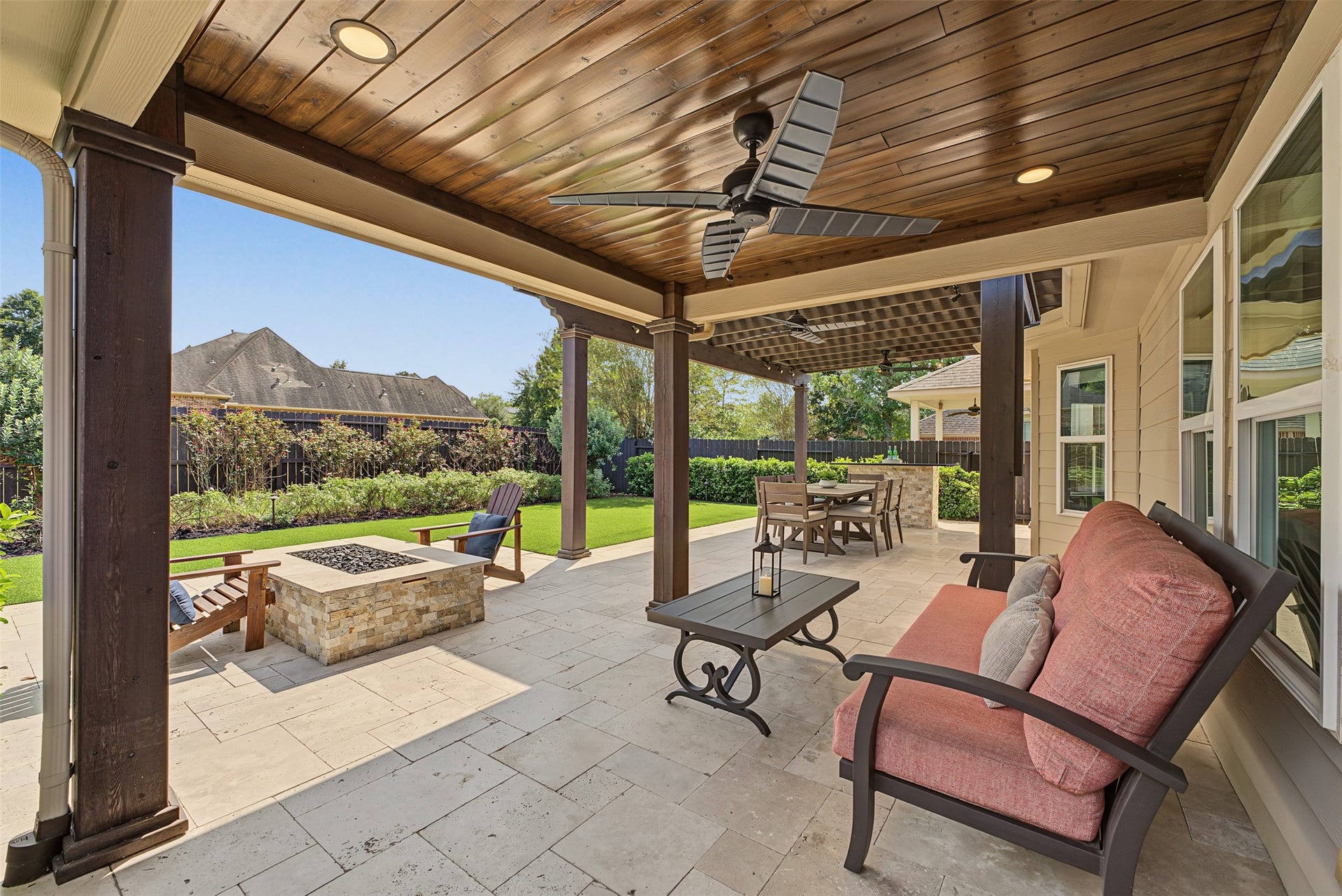 Experience outdoor living at its finest with this elegant covered patio, featuring a cozy seating area, ceiling fan, and a stylish fire pit, perfect for entertaining or relaxing in comfort.