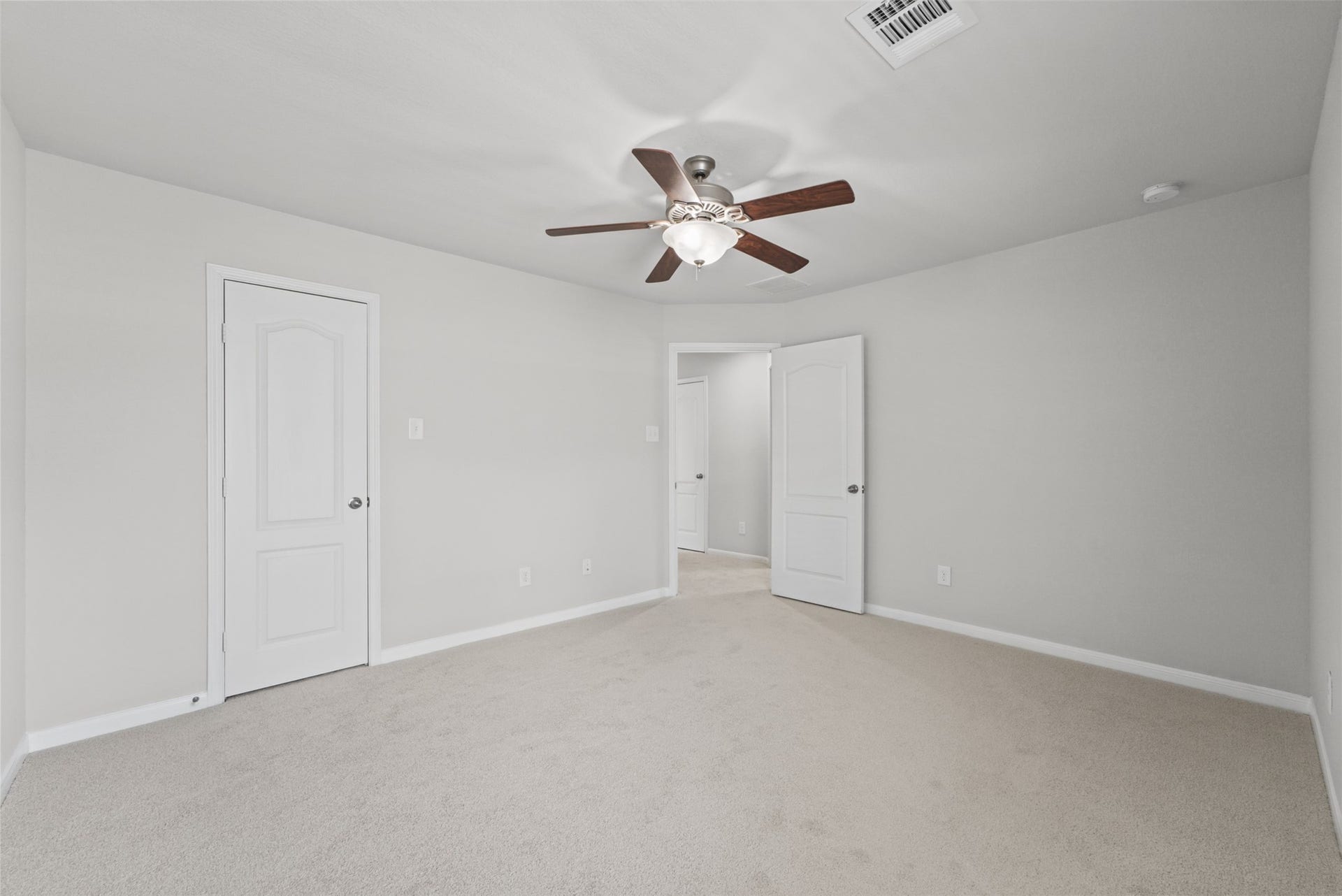 Spacious secondary bedroom with neutral carpeting and walls, featuring a ceiling fan and ample natural light.