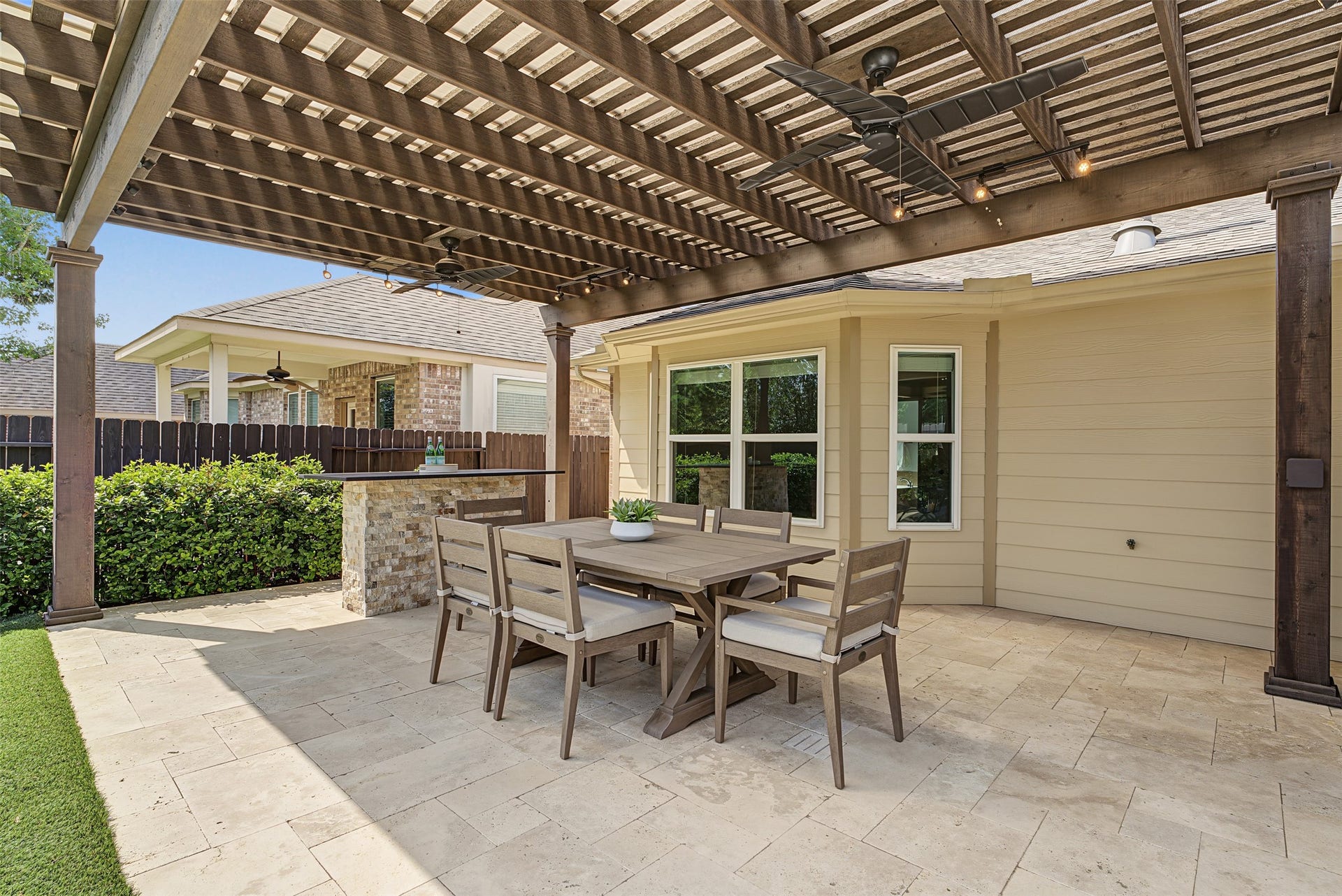 Charming outdoor patio with a stylish pergola, ceiling fans, and a spacious dining area, perfect for entertaining.
