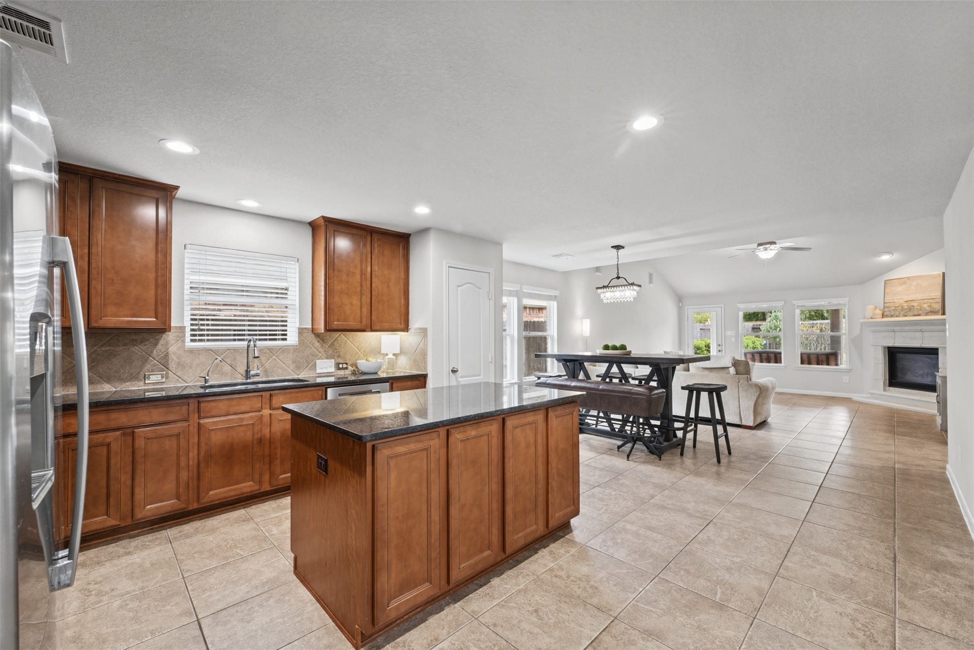 Spacious open-concept kitchen and living area featuring rich wooden cabinetry, a central island, cozy fireplace, and abundant natural light from large windows.
