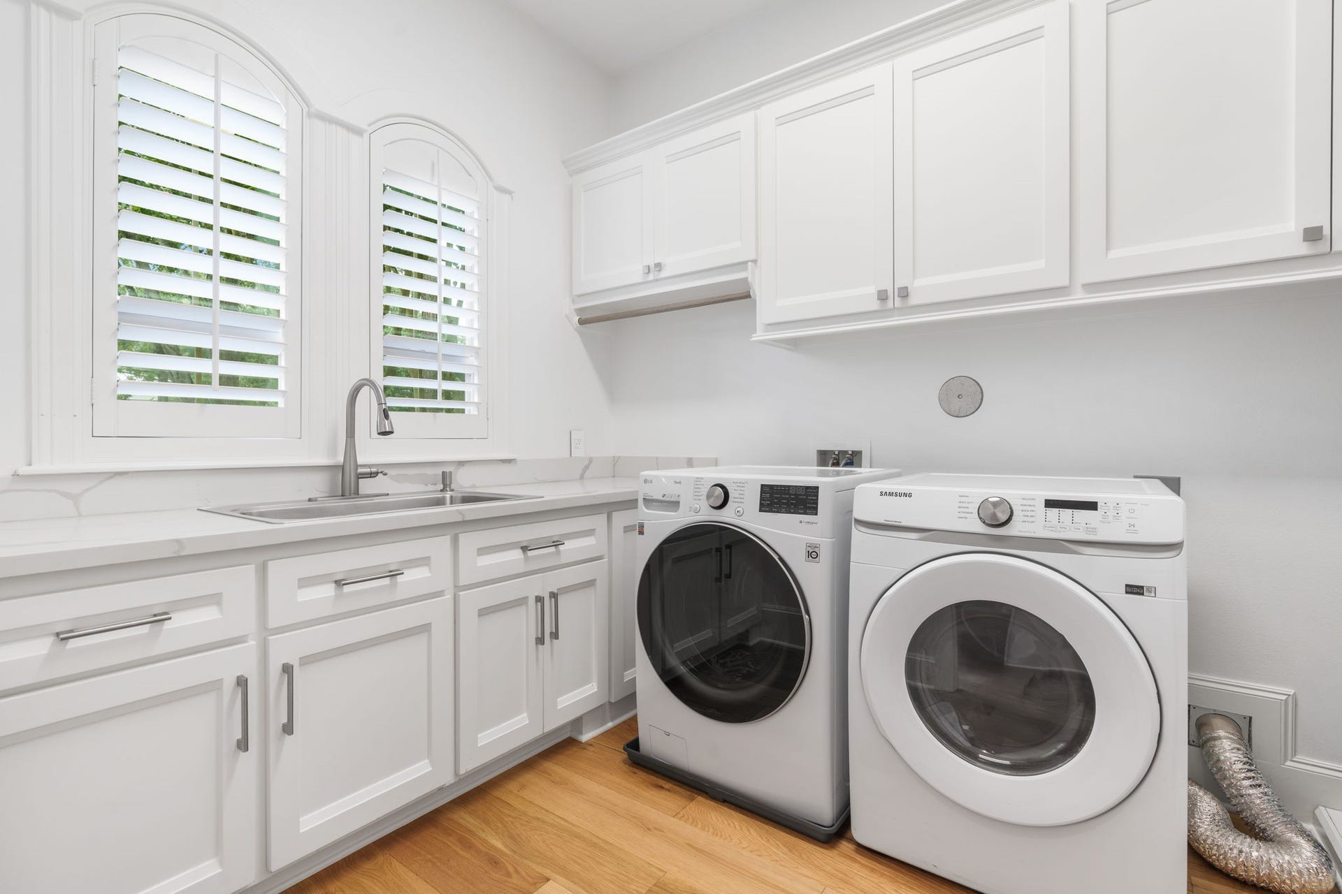 39 N Palmiera Circle, The Woodlands, TX 77382 A full utility room done right arched, plantation-shuttered windows over a stainless steel sink, quartz counters with plenty of prep space, built-in ironing board, floor-to-ceiling white cabinetry for storage, and easy care engineered flooring.