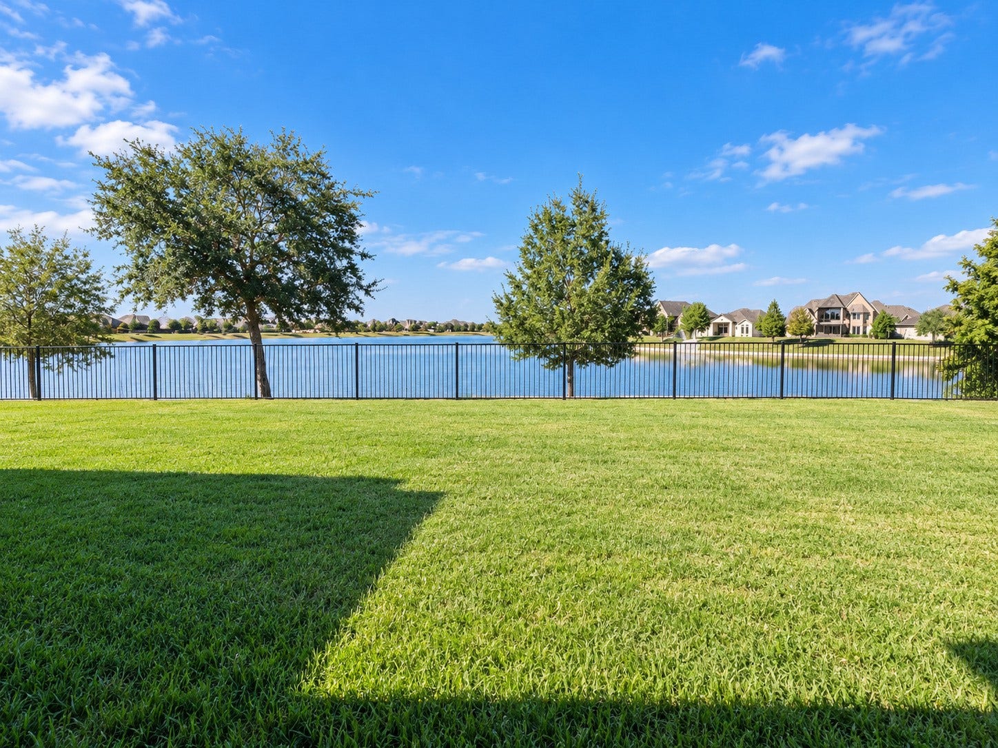 3414 Magnolia Shores Lane, Pearland, TX 77584 Expansive backyard overlooking the neighborhood lake, complete with mature trees and wrought-iron-style fencing.