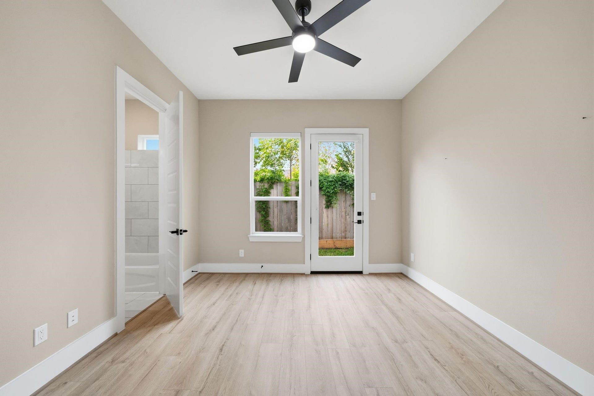 4013 Griggs Road, #F, Houston, TX 77021 Bright room with light wood flooring, a ceiling fan, and access to a private outdoor area through a glass door. Adjacent bathroom entry enhances convenience.