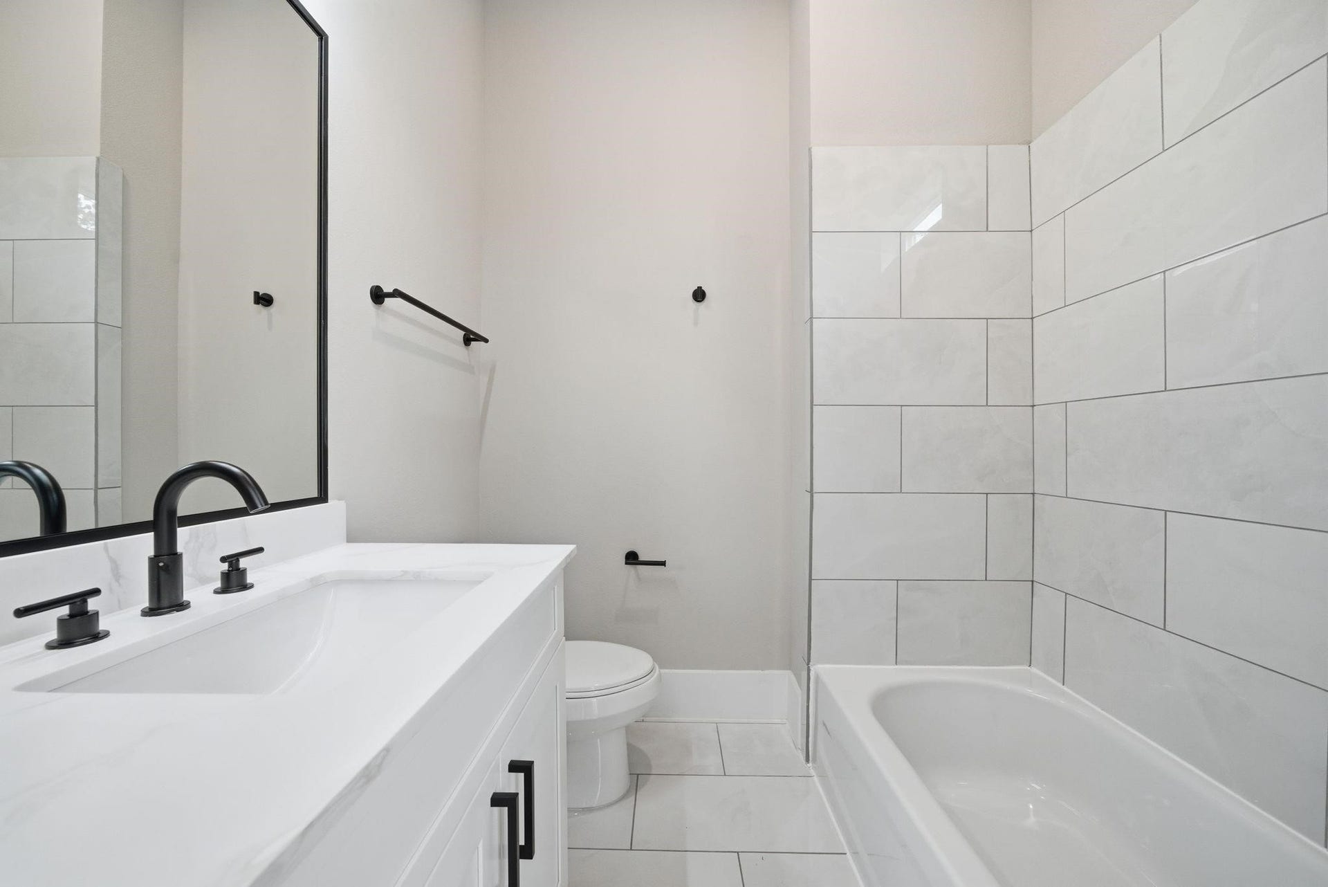 4013 Griggs Road, #F, Houston, TX 77021 Sleek bathroom featuring a modern vanity with dual faucets, a large mirror, and a pristine tub surrounded by elegant white tiling.