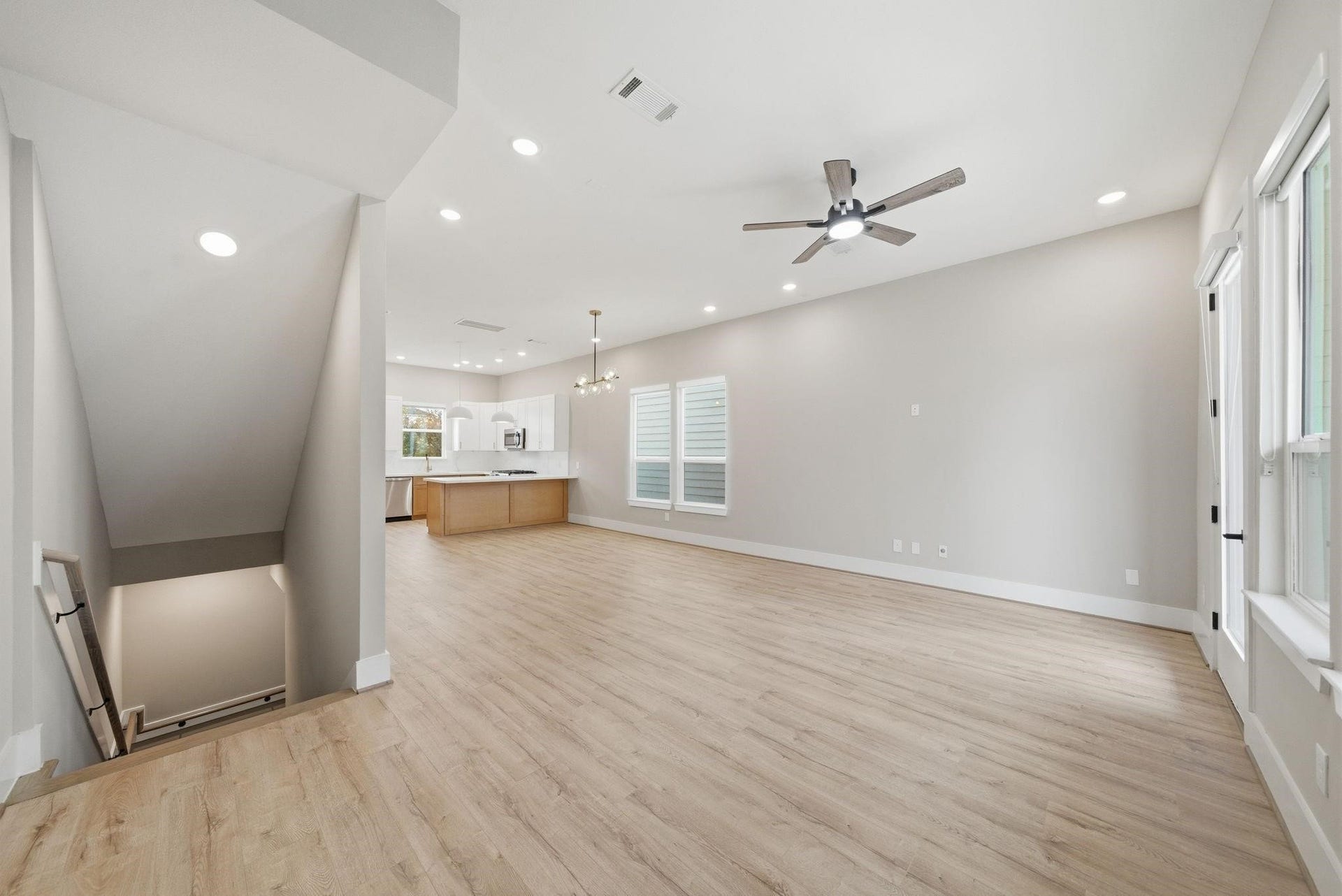 4013 Griggs Road, #F, Houston, TX 77021 Spacious open-concept living area with sleek wood flooring, recessed lighting, and a modern ceiling fan, seamlessly flowing into a bright kitchen with white cabinetry and an island.