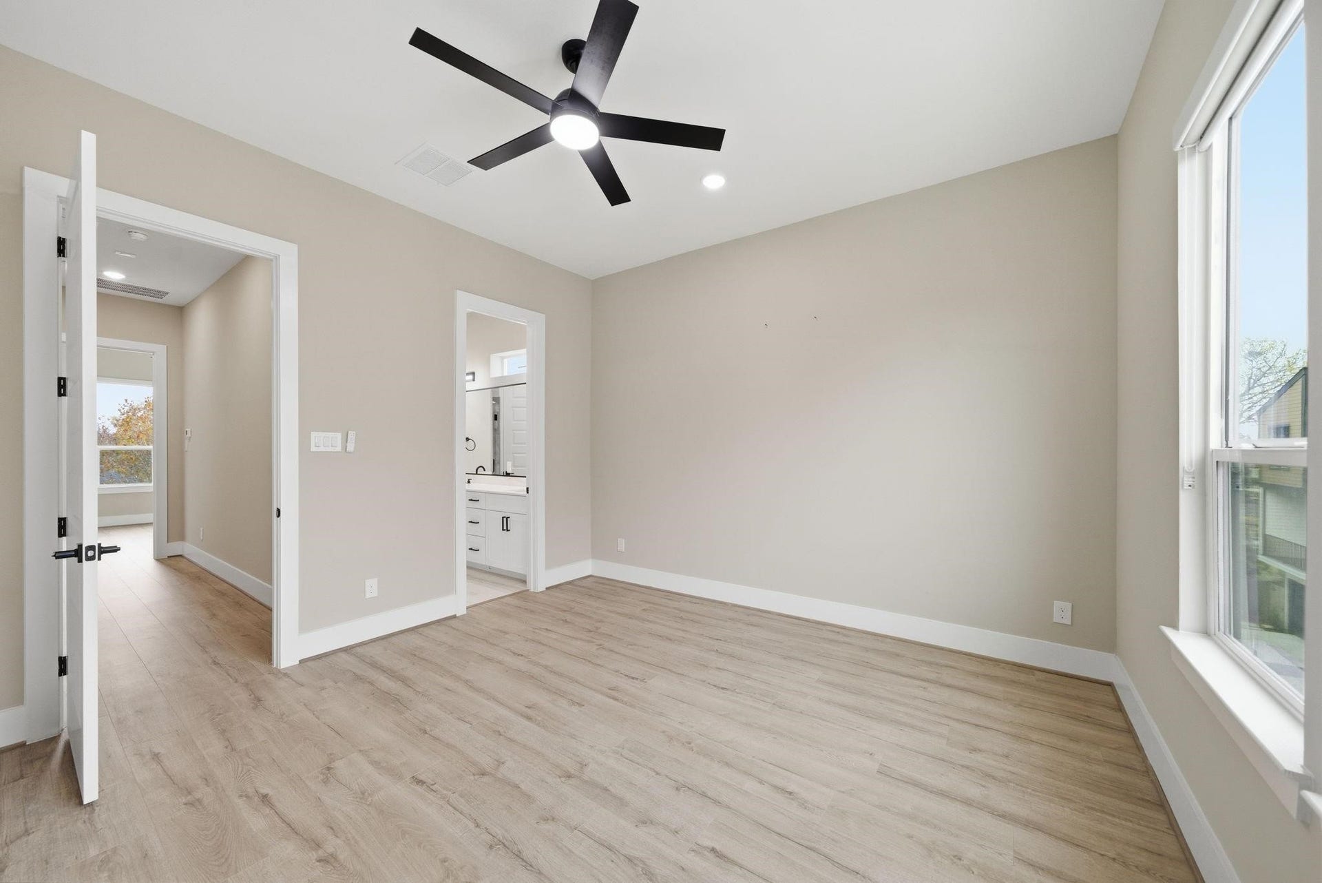 4013 Griggs Road, #F, Houston, TX 77021 Bright and spacious bedroom featuring sleek hardwood floors, a modern ceiling fan, and ample natural light from large windows, with convenient access to a stylish en-suite bathroom.