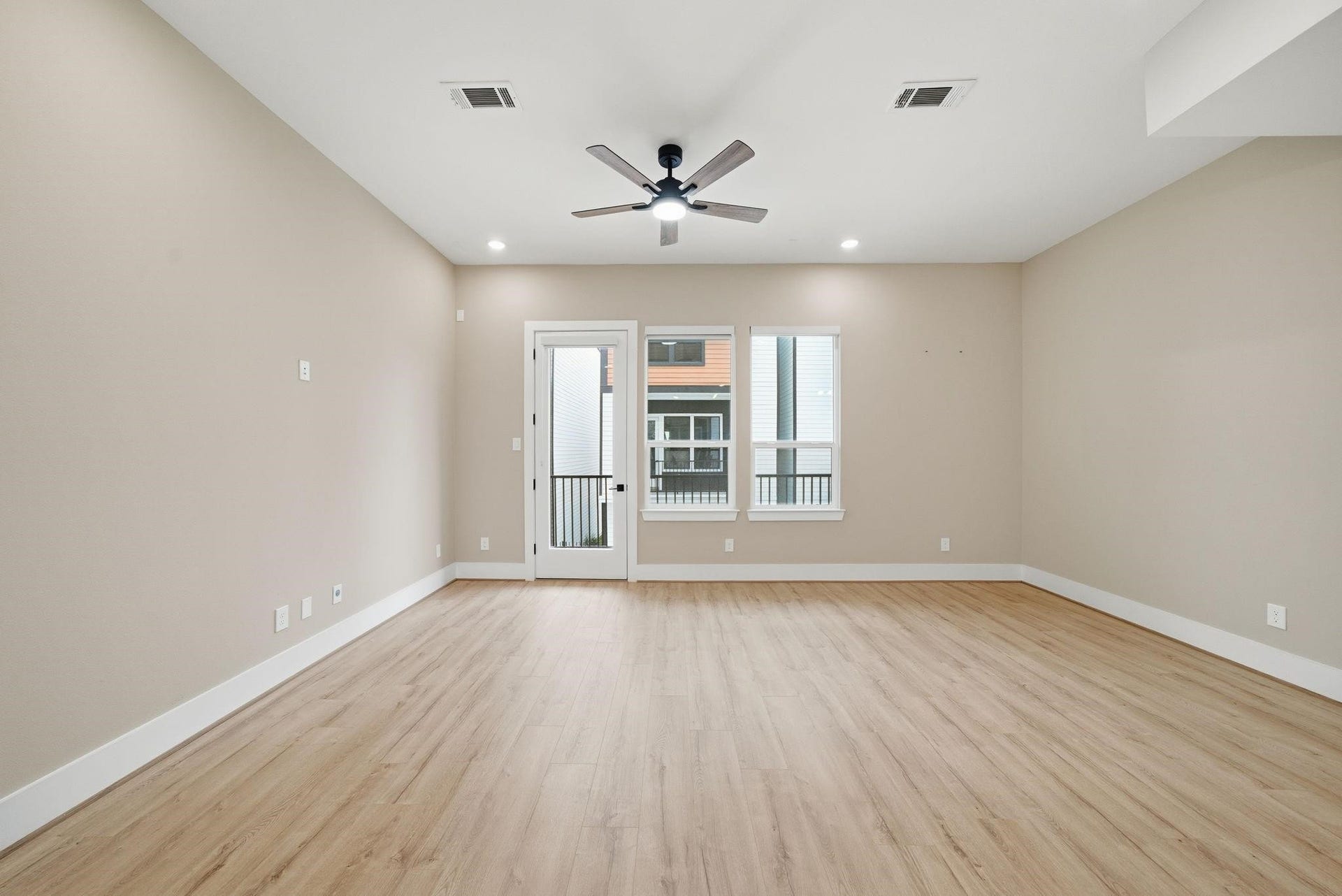 4013 Griggs Road, #F, Houston, TX 77021 Spacious living area with sleek wood flooring, neutral walls, and abundant natural light from large windows and a glass door leading to a small balcony.