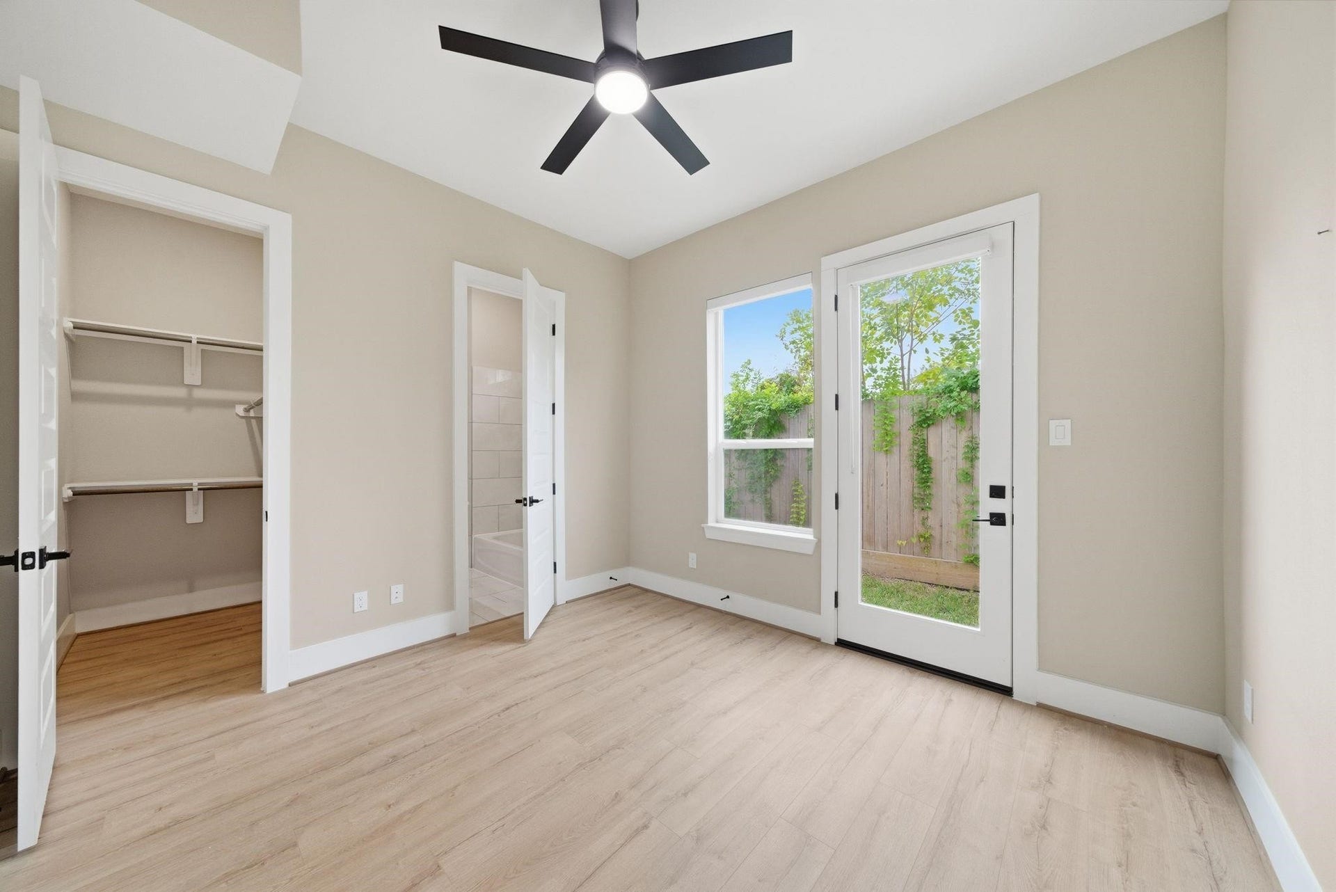 4013 Griggs Road, #F, Houston, TX 77021 Bright and airy bedroom featuring sleek wood flooring, a ceiling fan, and direct access to the backyard through elegant French doors.