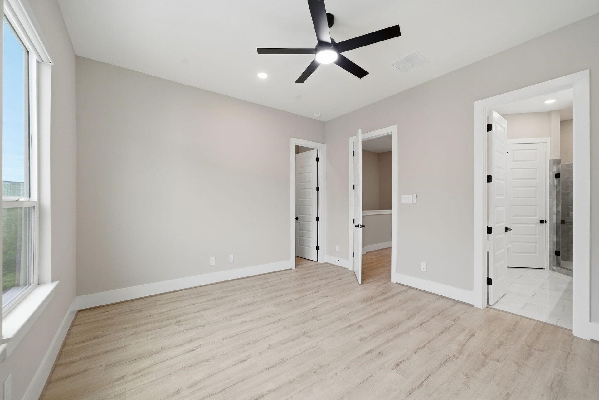 4013 Griggs Road, #F, Houston, TX 77021 Bright and inviting bedroom featuring sleek hardwood floors, a modern ceiling fan, and abundant natural light from large windows, leading to an en-suite bathroom with stylish finishes.