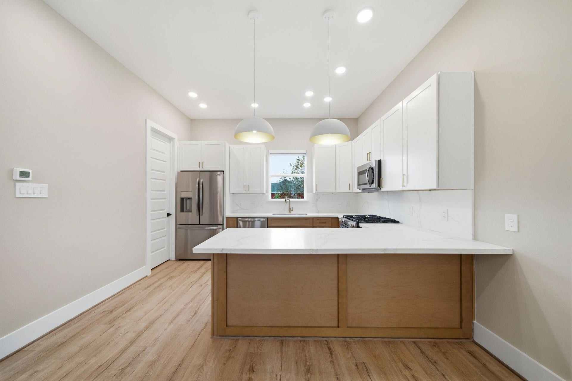 4013 Griggs Road, #F, Houston, TX 77021 Modern kitchen featuring sleek white cabinetry, stainless steel appliances, and a spacious island with pendant lighting, set against beautiful wood flooring.