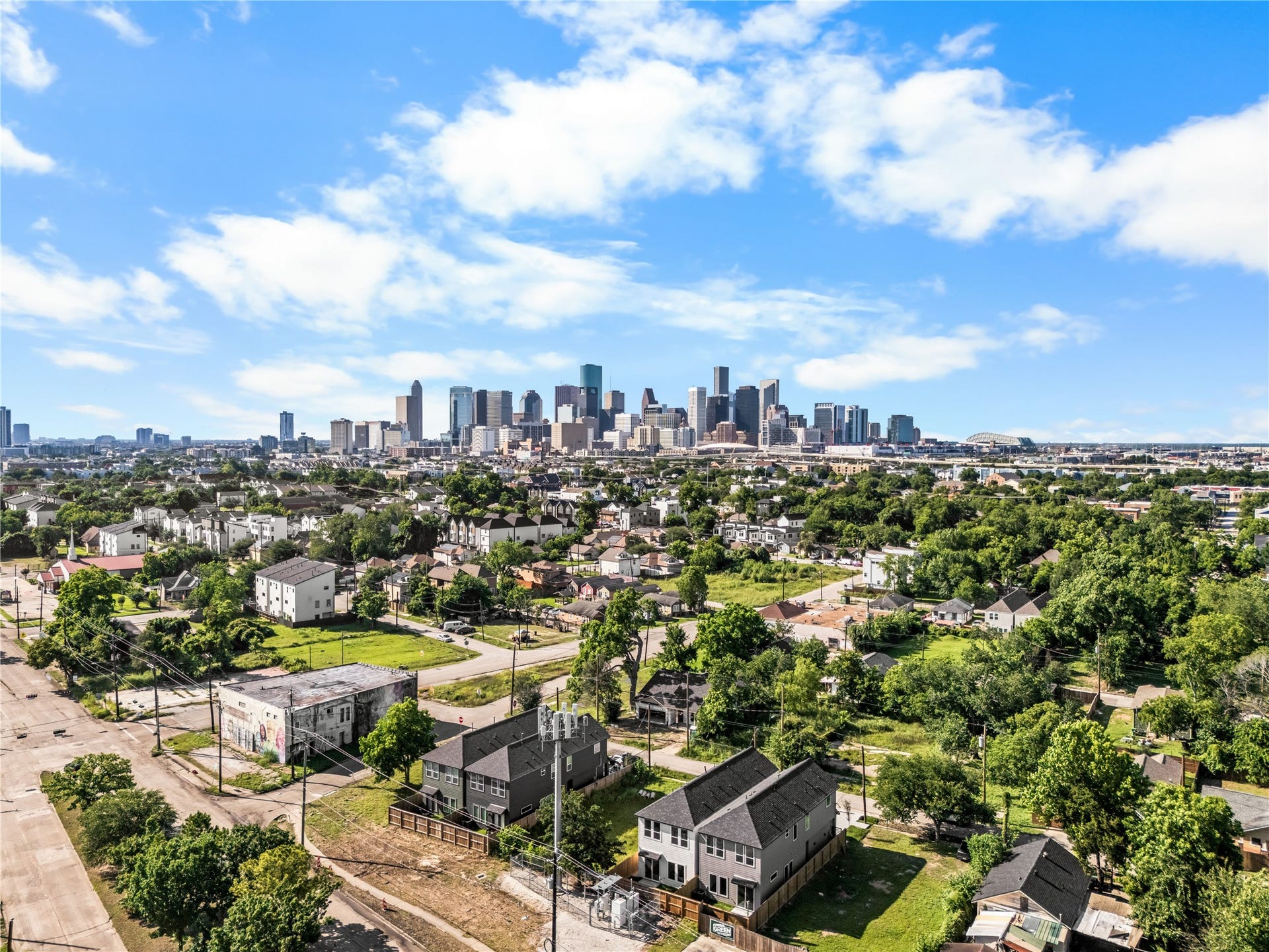 3012 & 3014 Beulah St, Houston, TX 77004 This drone view shows the home's proximity to downtown, nestled in a residential neighborhood surrounded by mature trees. Under a clear blue sky, the property offers an unobstructed view of the city skyline, highlighting its balance of neighborhood charm and urban access.
