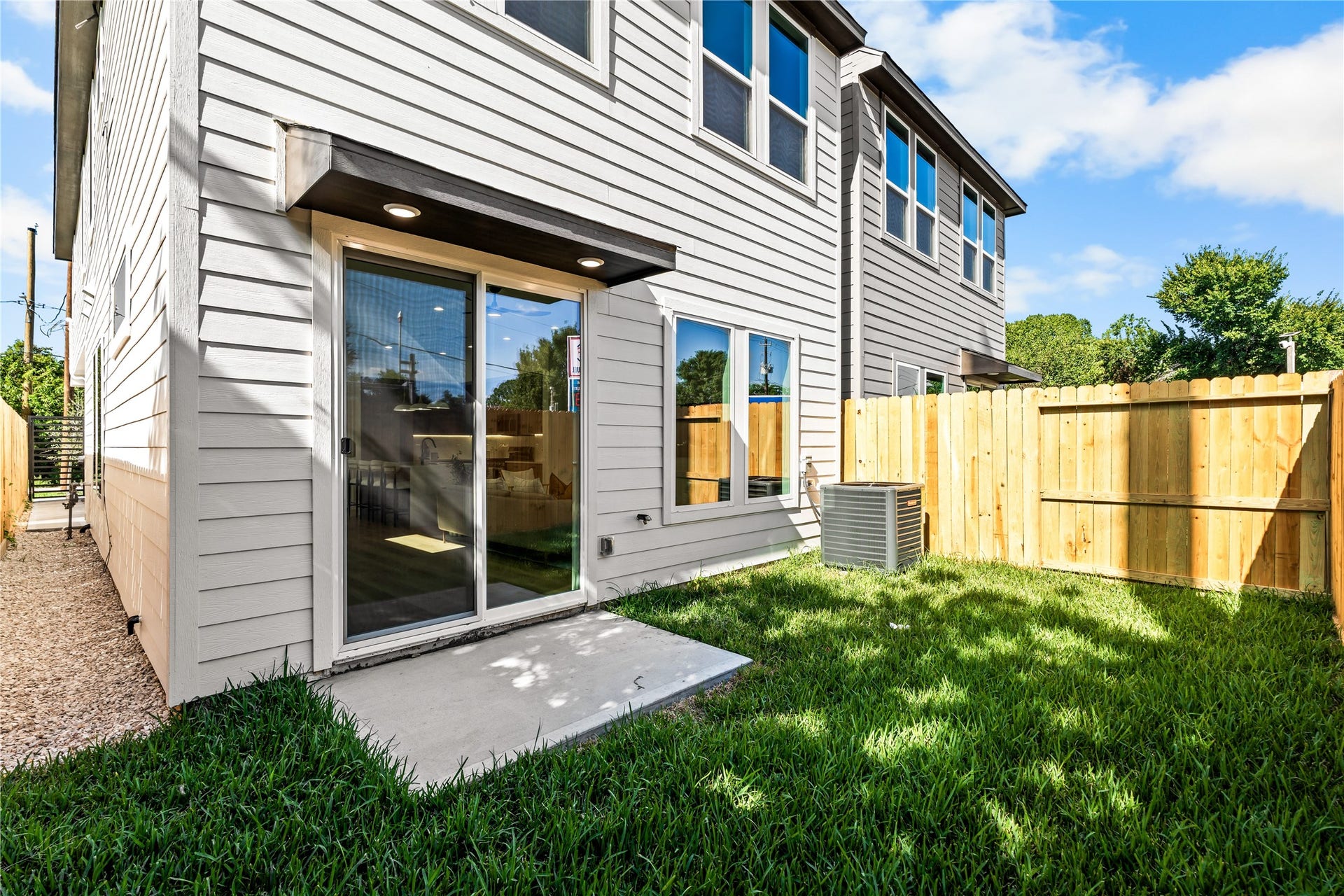 3012 & 3014 Beulah St, Houston, TX 77004 The private, fully fenced backyard features a manicured green lawn and a concrete patio for outdoor seating and grilling. Surrounded by a wooden privacy fence, the space includes a modern HVAC compressor and a covered awning with recessed lighting above massive sliding glass doors that lead inside.