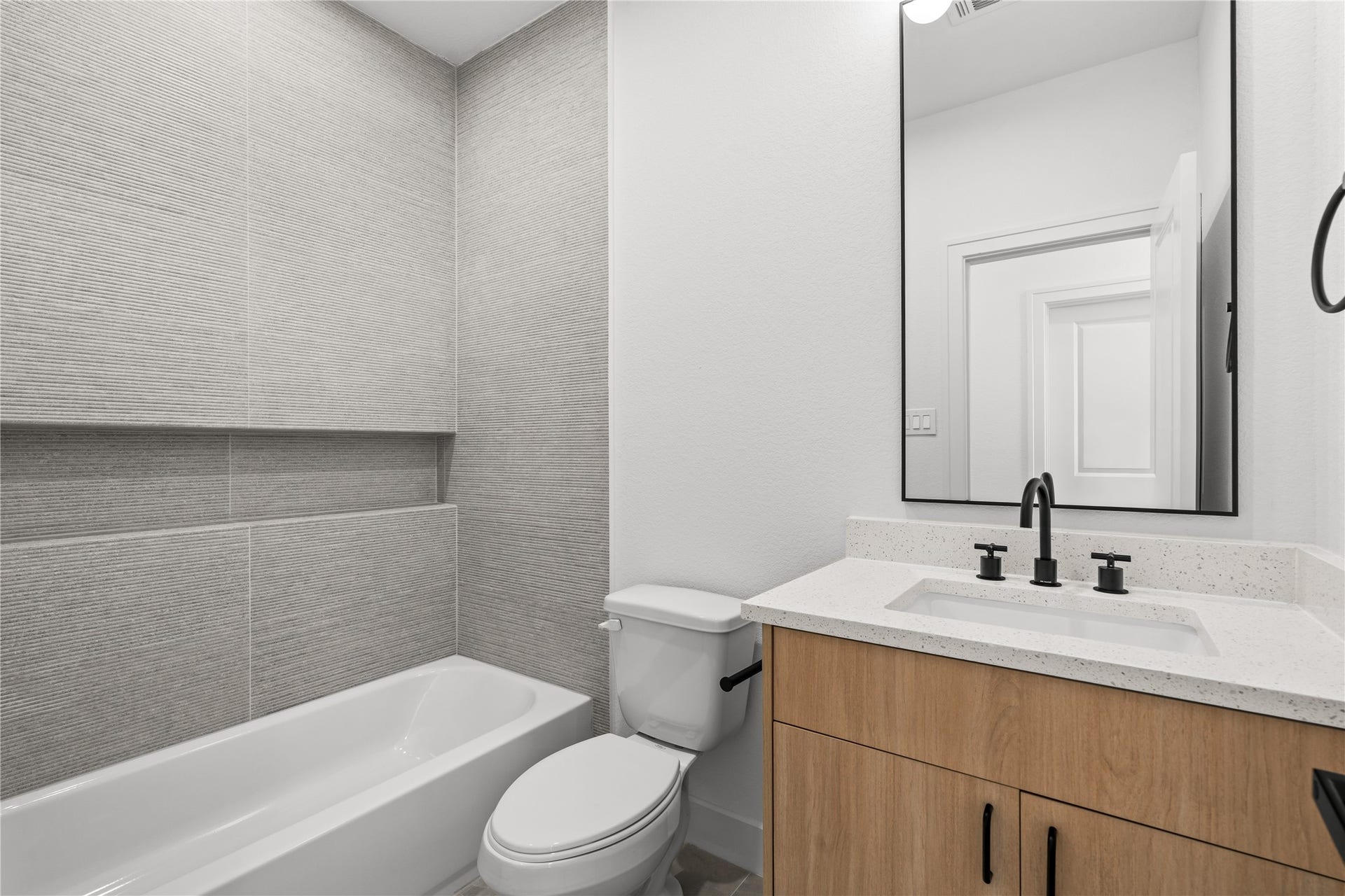 3012 & 3014 Beulah St, Houston, TX 77004 The adjacent full bathroom features a wood vanity with a white quartz countertop, an under-mount sink, and a black-framed mirror. A black gooseneck faucet pairs with the mirror, while the shower-tub combination is lined with neutral horizontal tiles.