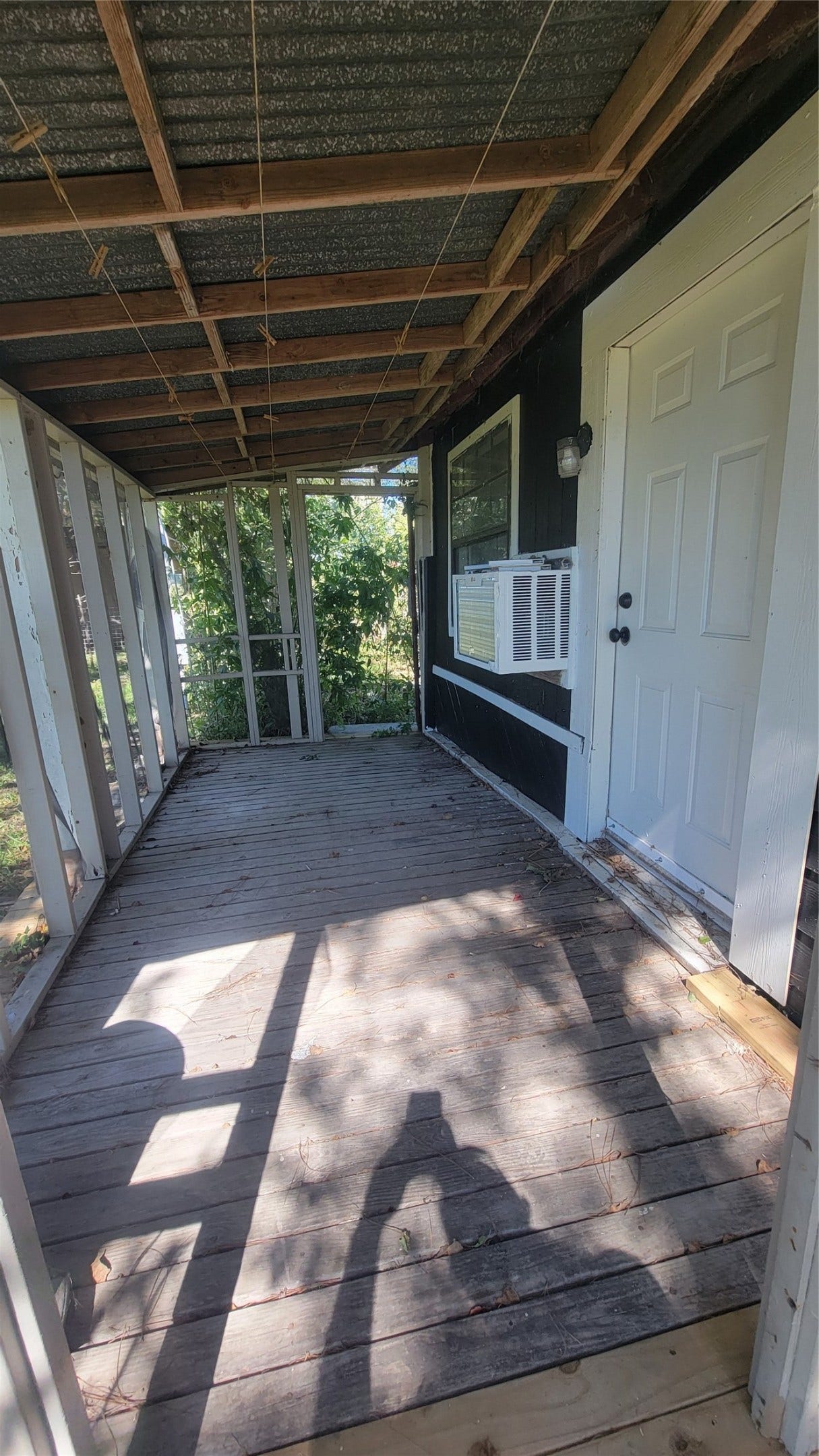 12018 Sandpiper Road, Angleton, TX 77515 This photo showcases a rustic, covered porch with a wooden floor and open railing, featuring a side door and a window AC unit. The porch is shaded, providing a cozy outdoor space.