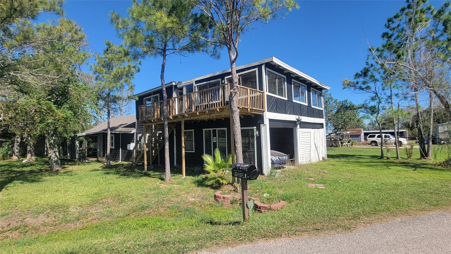 12018 Sandpiper Road, Angleton, TX 77515 Two-story home with a wooden balcony and large windows, set in a grassy yard with mature trees. The property includes a garage and has a driveway leading to the street.