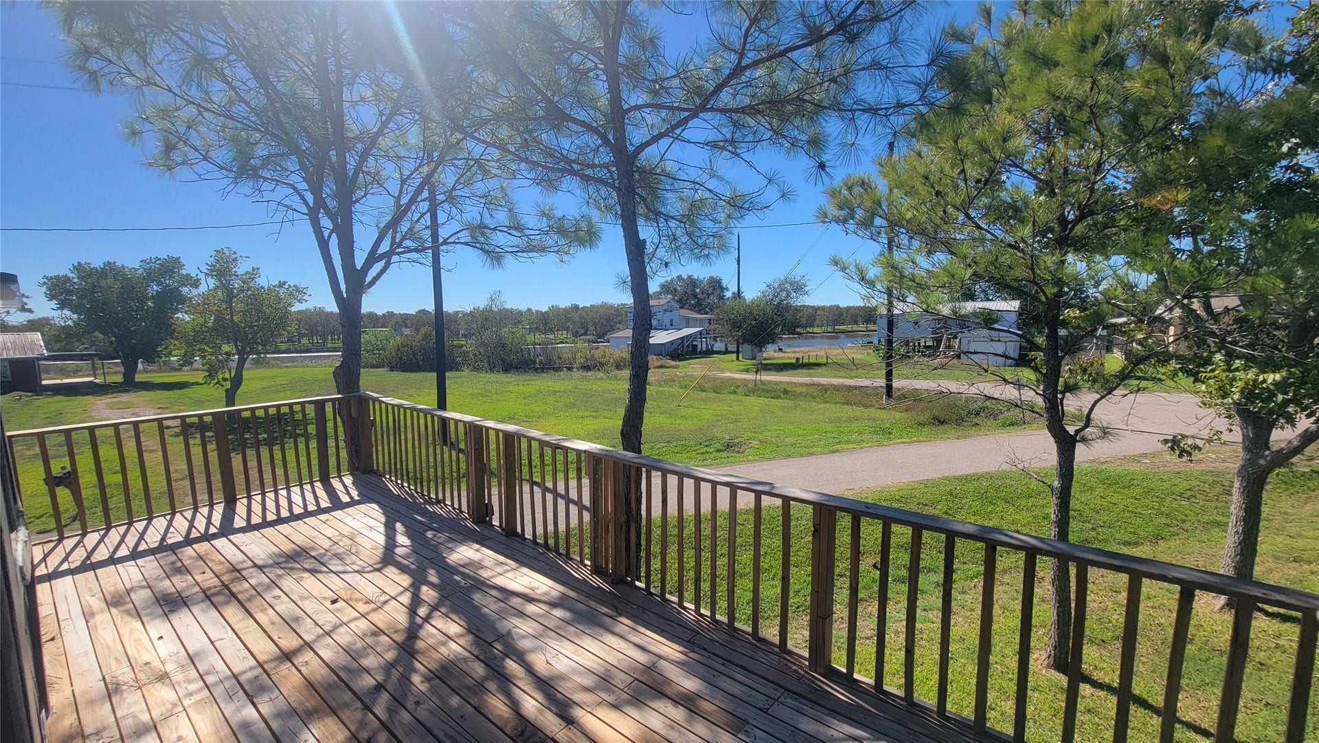 12018 Sandpiper Road, Angleton, TX 77515 This photo showcases a spacious wooden deck overlooking a lush green yard with mature trees, offering a serene and private outdoor space with a countryside view.