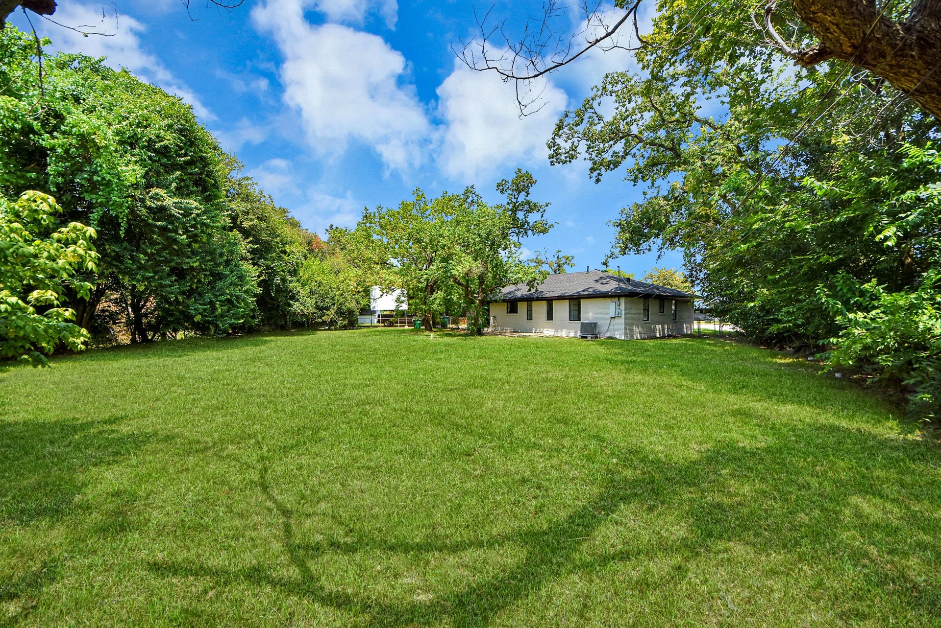 602 Gammon Drive, Houston, TX 77022 Expansive green backyard surrounded by mature trees, offering privacy and tranquility with a cozy single-story home nestled in the corner.