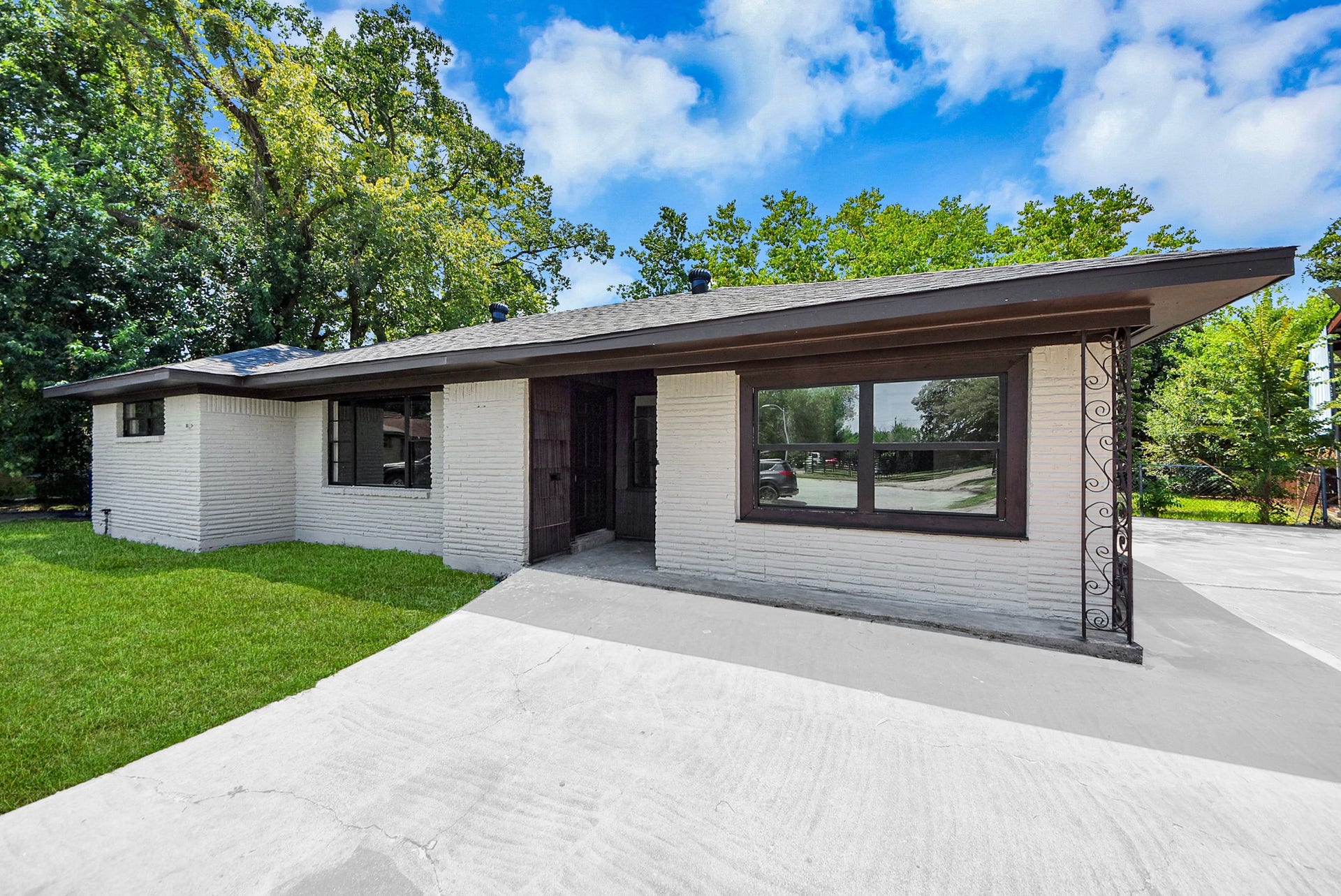 602 Gammon Drive, Houston, TX 77022 Charming single-story home with a sleek white brick exterior, large windows, and a spacious driveway, set against a backdrop of lush greenery.