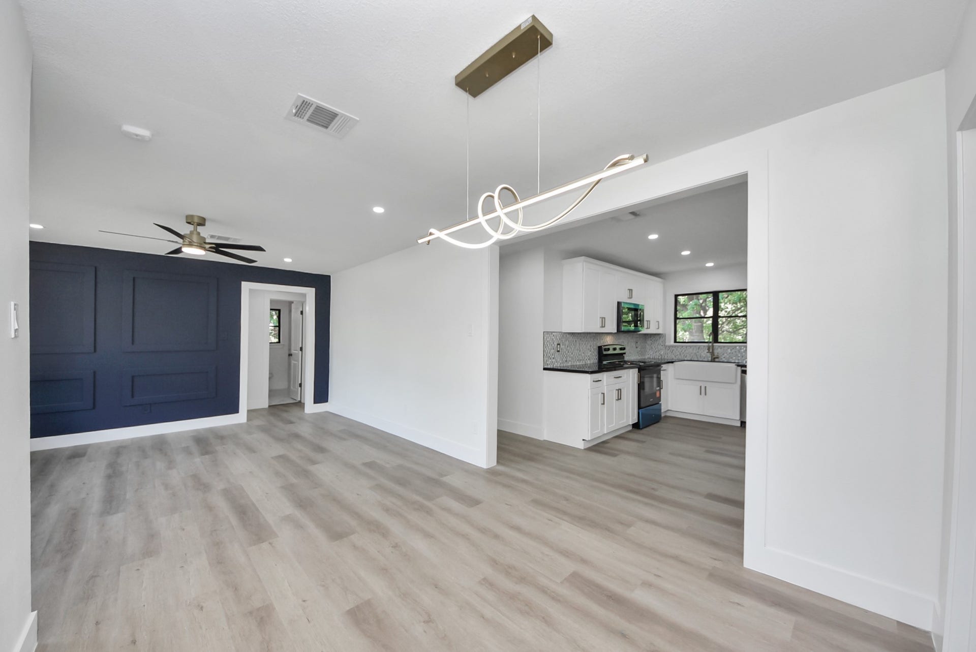 602 Gammon Drive, Houston, TX 77022 Experience modern elegance in this open-concept living space featuring sleek wood flooring, a striking navy accent wall, and a contemporary light fixture. The adjoining kitchen is beautifully appointed with white cabinetry and stylish backsplash, perfect for entertaining.