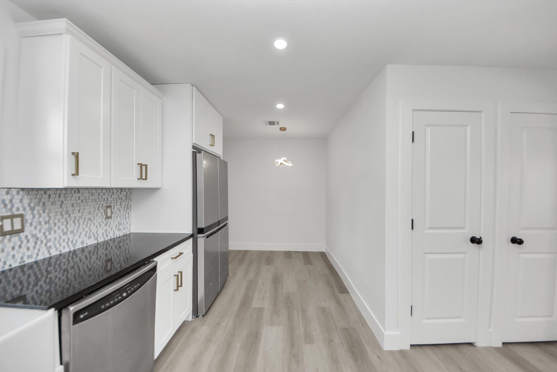 602 Gammon Drive, Houston, TX 77022 Modern kitchen with sleek white cabinetry, stainless steel appliances, and elegant black countertops, complemented by a stylish mosaic backsplash and chic lighting.