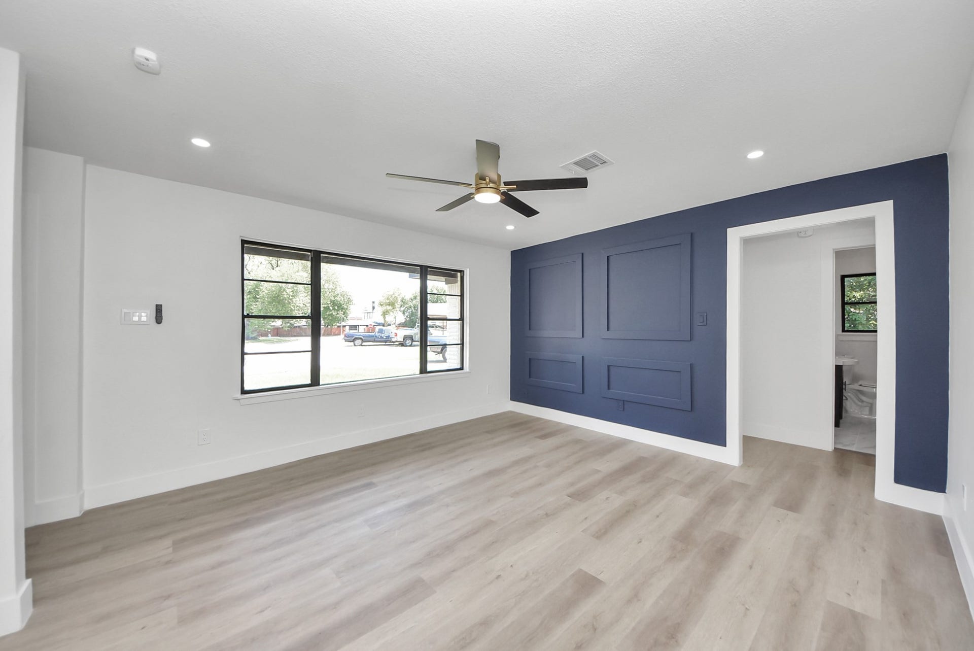 602 Gammon Drive, Houston, TX 77022 Bright and modern living area featuring a stylish accent wall, large windows, and sleek wood flooring, complemented by a contemporary ceiling fan.