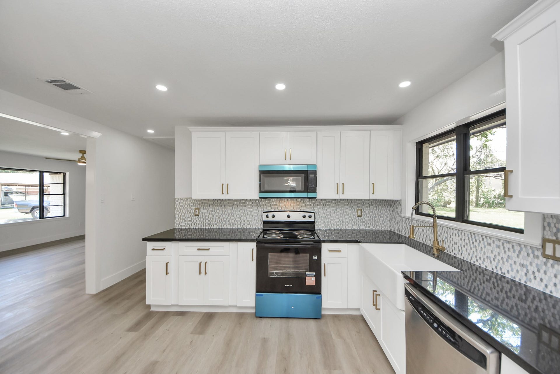 602 Gammon Drive, Houston, TX 77022 Sleek and modern kitchen featuring stainless steel appliances, elegant white cabinetry, and a stylish mosaic backsplash, complemented by a spacious farmhouse sink and ample natural light from large windows.