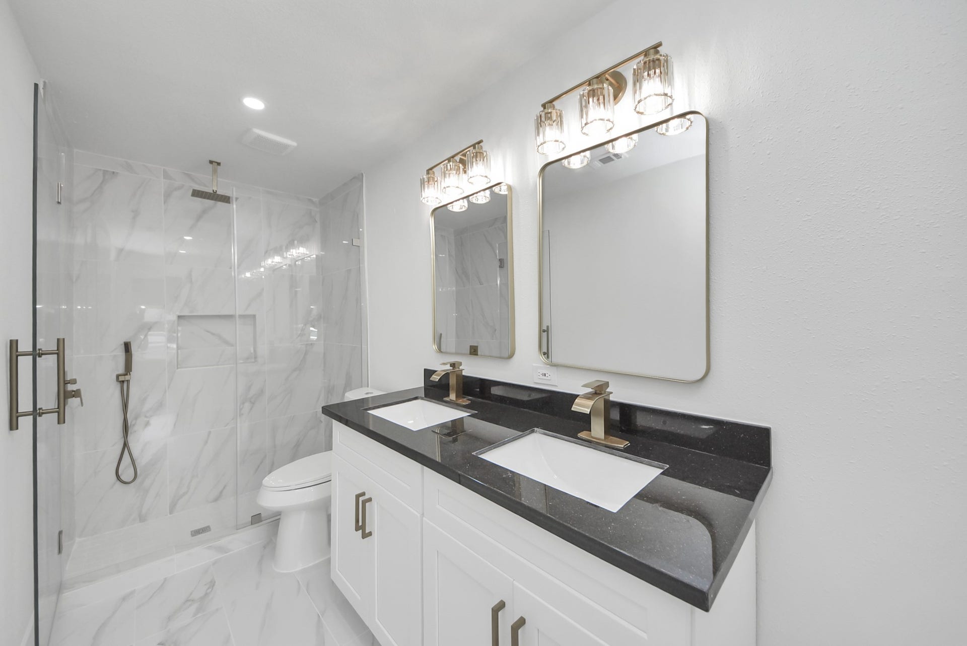 602 Gammon Drive, Houston, TX 77022 Elegant bathroom featuring a sleek double vanity with black countertops, gold fixtures, and a spacious glass-enclosed shower with modern tilework.