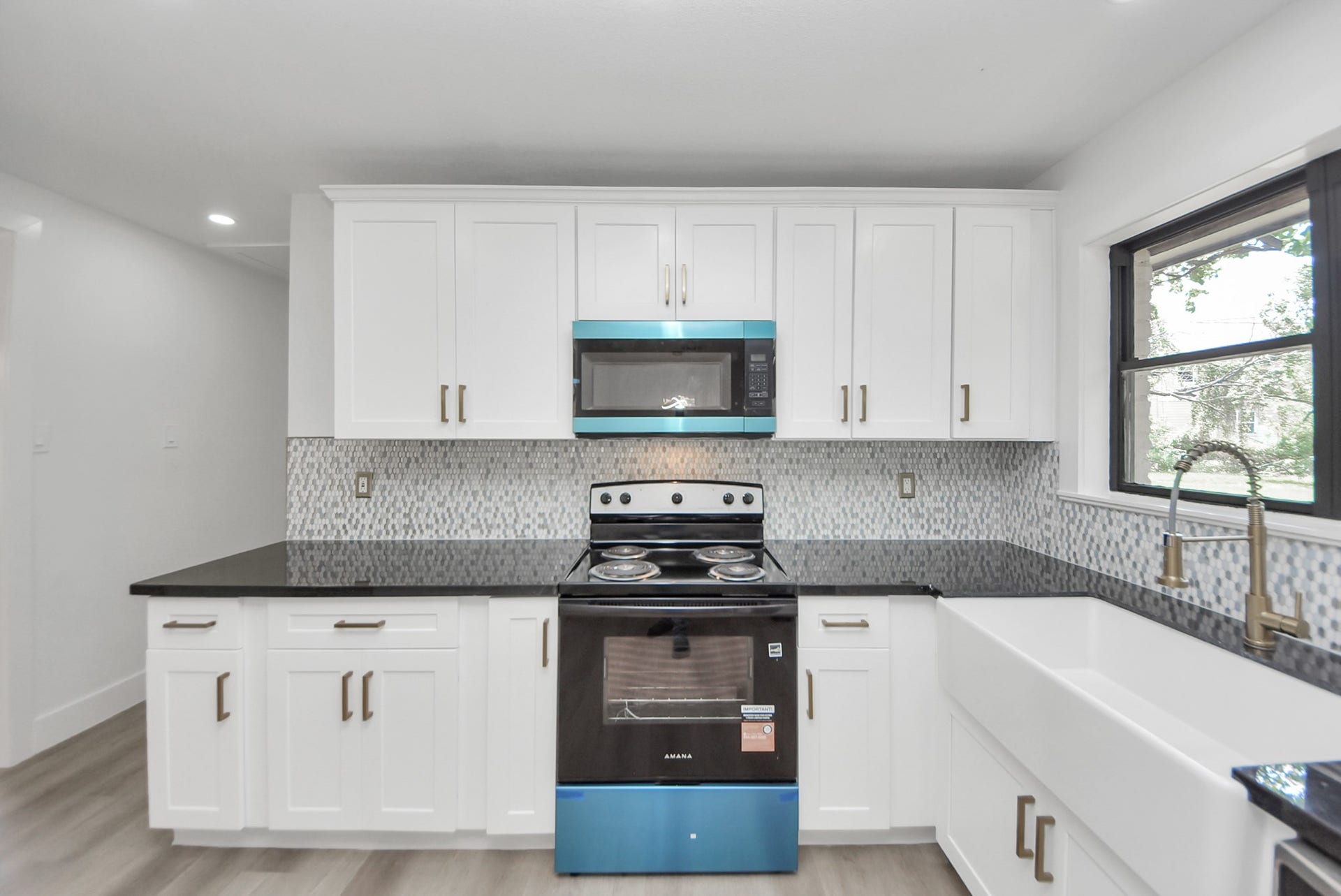602 Gammon Drive, Houston, TX 77022 Sleek kitchen featuring modern appliances, crisp white cabinetry, and elegant black countertops, complemented by a stylish tile backsplash and a spacious farmhouse sink.