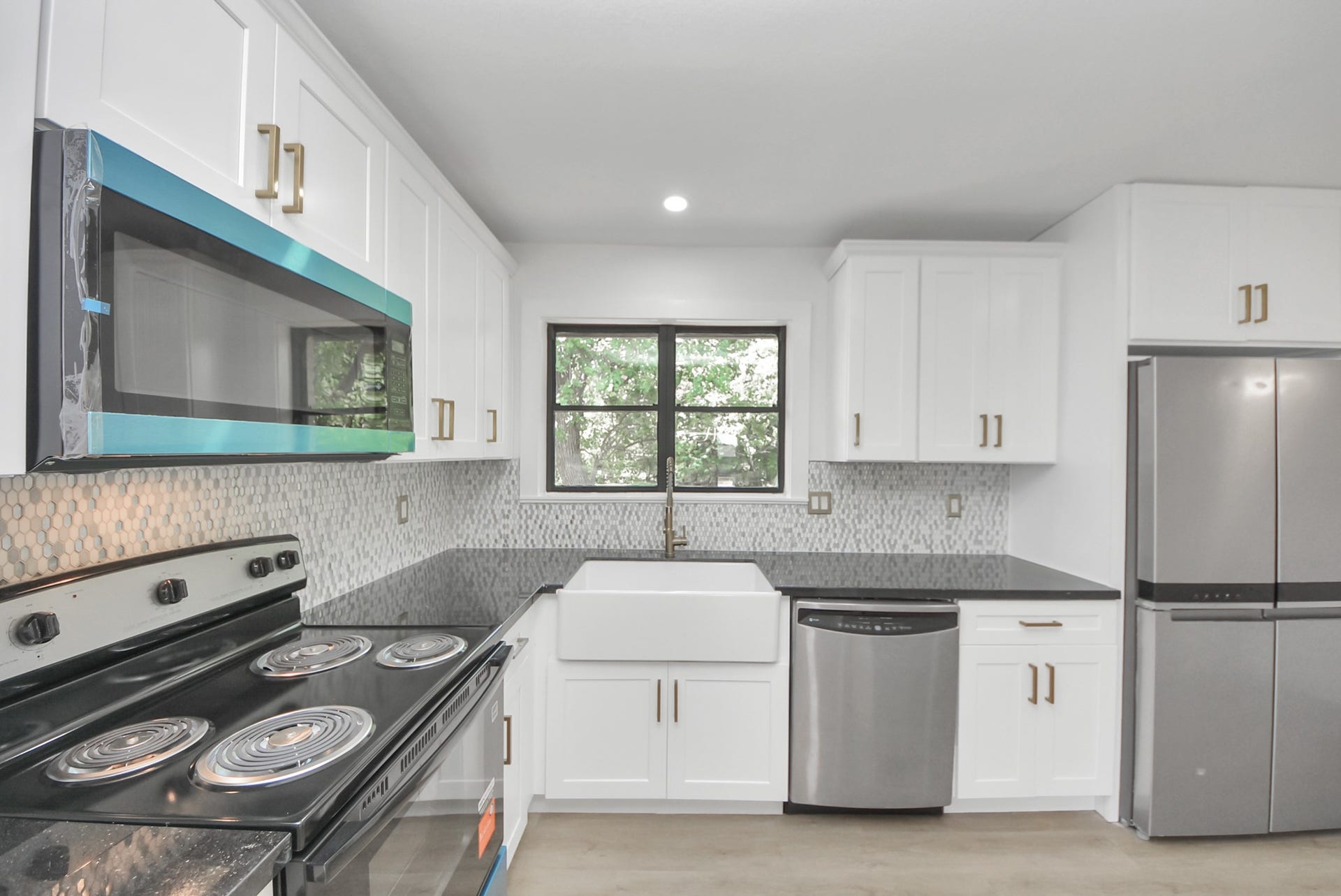 602 Gammon Drive, Houston, TX 77022 Charming kitchen with modern appliances, sleek black countertops, and a stylish farmhouse sink. Bright white cabinetry complements the mosaic tile backsplash, creating a fresh and inviting atmosphere.