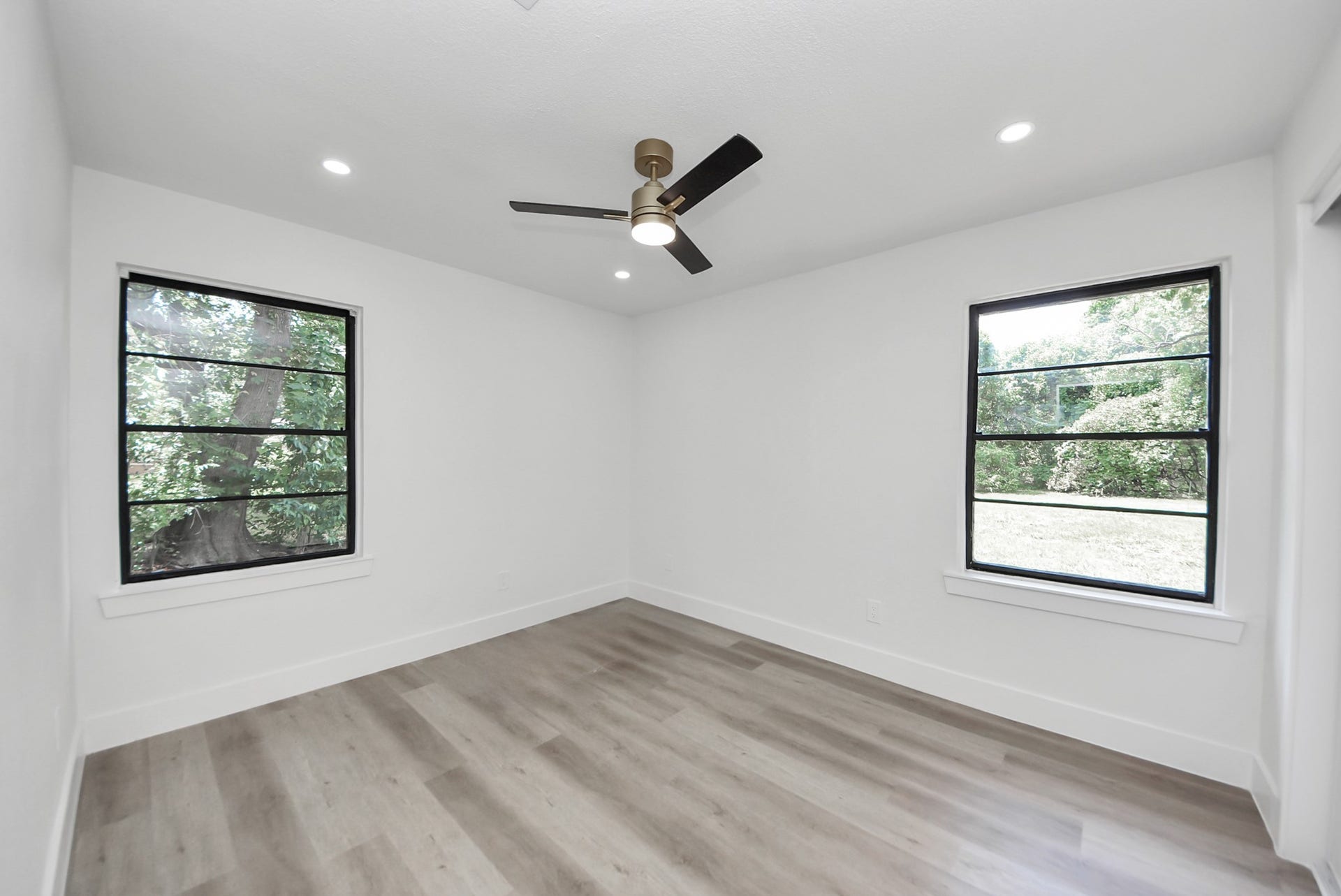 602 Gammon Drive, Houston, TX 77022 Bright and airy bedroom featuring large windows with tranquil views, sleek hardwood flooring, and a modern ceiling fan.