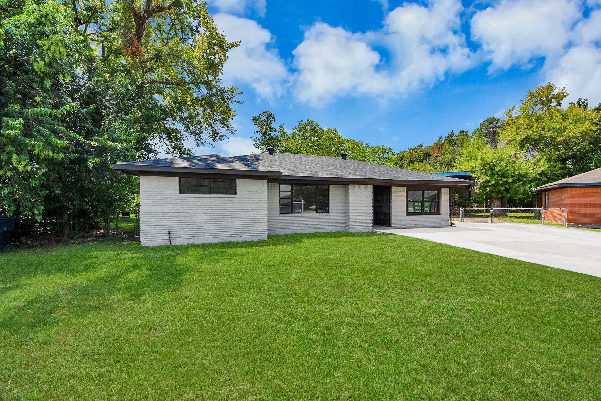 602 Gammon Drive, Houston, TX 77022 Charming brick ranch-style home with a spacious front yard and a sleek modern roof, surrounded by mature trees for added privacy and shade.