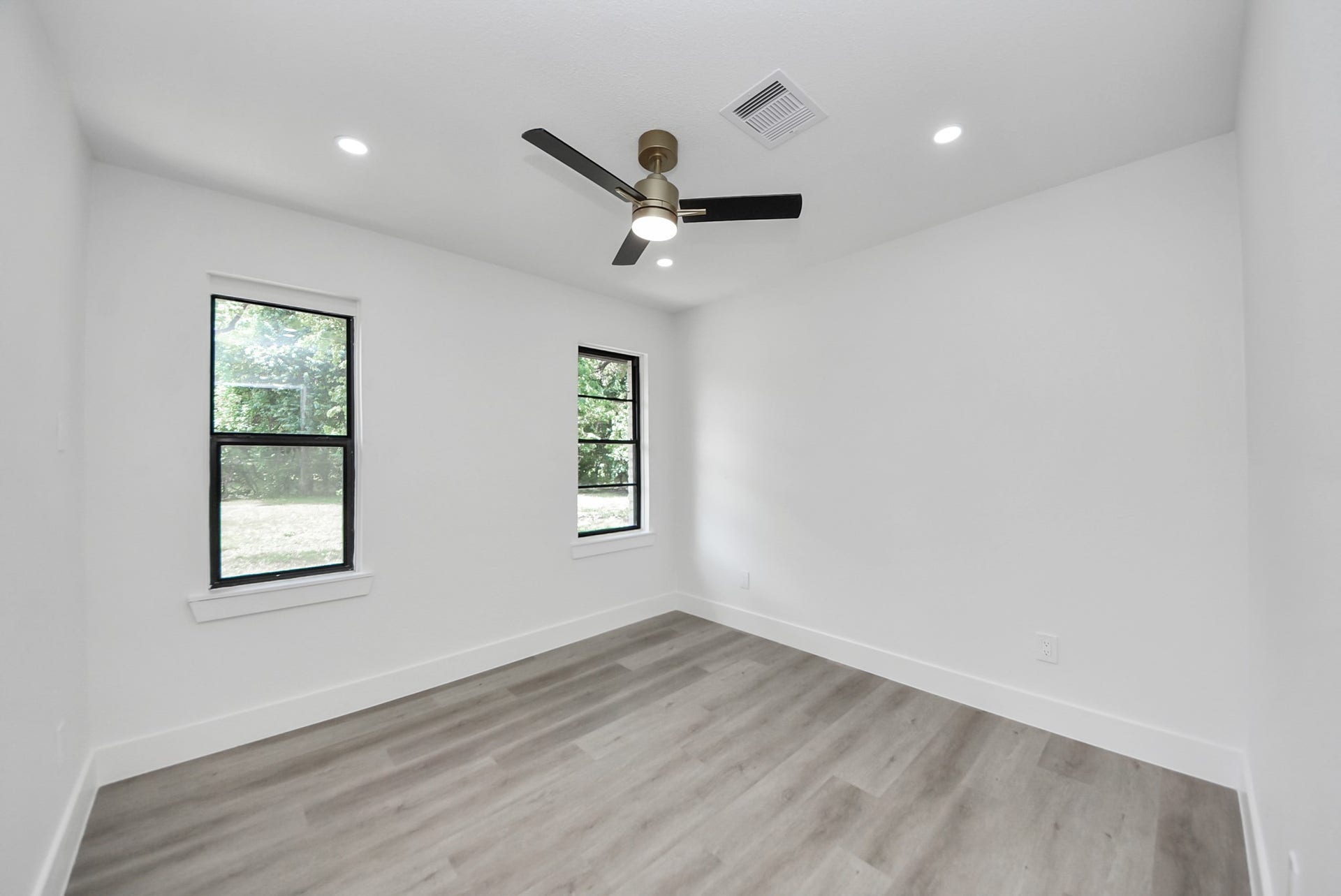 602 Gammon Drive, Houston, TX 77022 Bright and airy room featuring sleek laminate flooring, fresh white walls, and large windows offering serene outdoor views, complemented by a modern ceiling fan for comfort.
