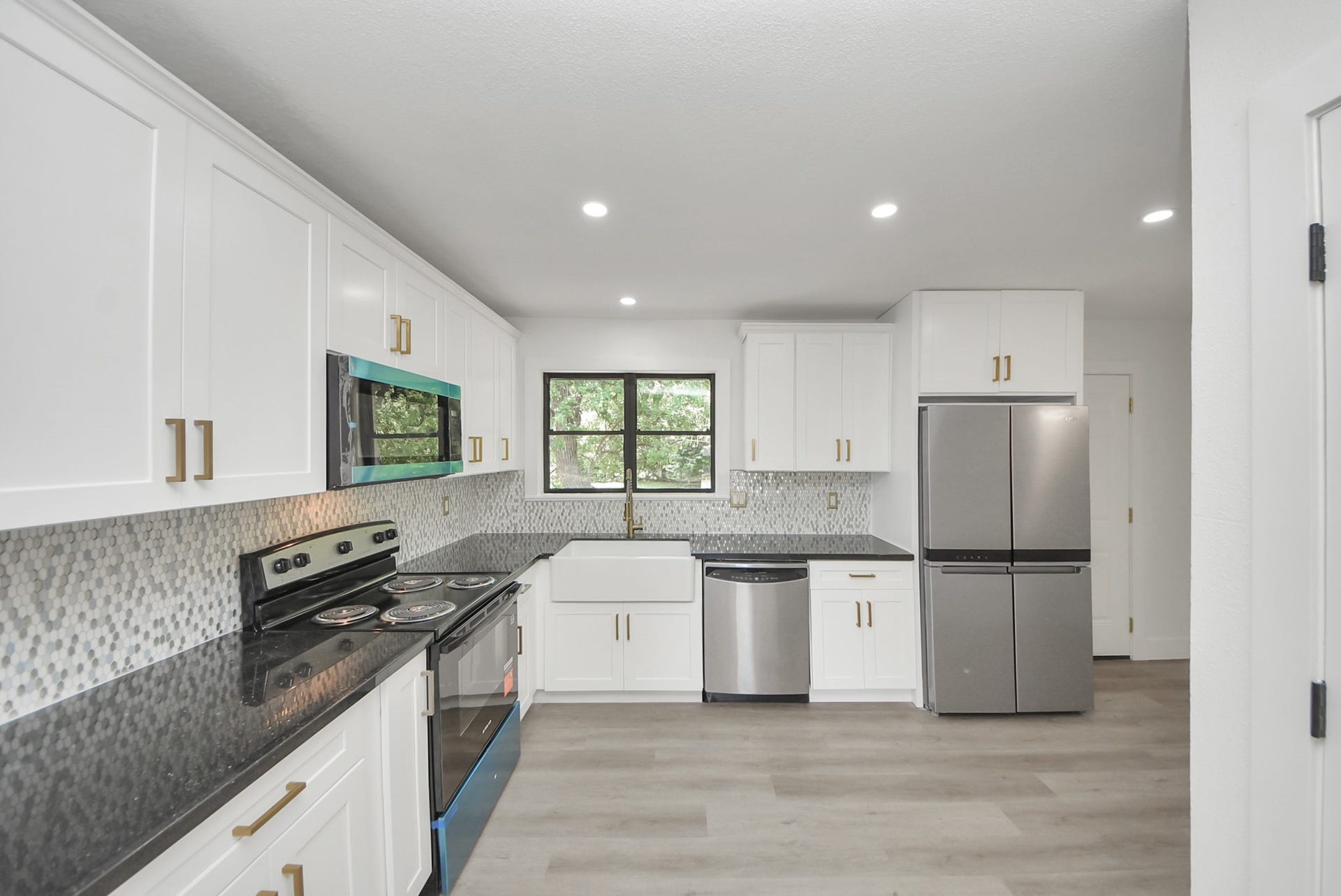602 Gammon Drive, Houston, TX 77022 Modern kitchen featuring sleek white cabinetry, stainless steel appliances, and a stylish farmhouse sink. The elegant mosaic backsplash and dark countertops complement the bright, open space.