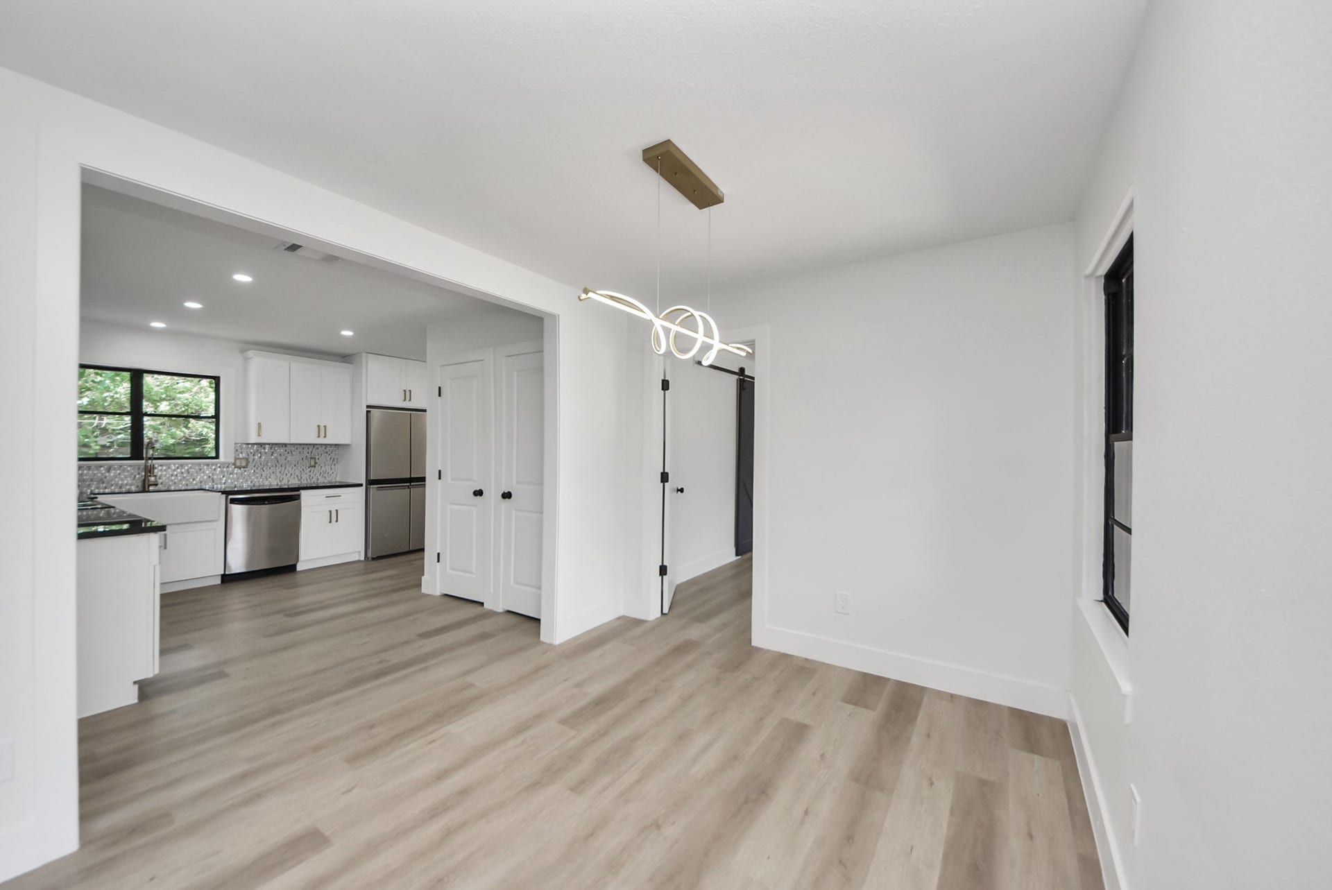 602 Gammon Drive, Houston, TX 77022 Bright and modern space with sleek light wood flooring, a contemporary light fixture, and an open view into a stylish kitchen featuring stainless steel appliances and a farmhouse sink.