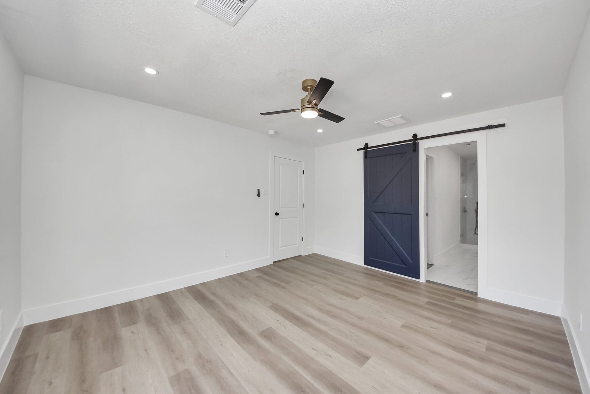 602 Gammon Drive, Houston, TX 77022 Spacious room with sleek wood flooring, recessed lighting, and a stylish ceiling fan. Features a modern barn door leading to an en-suite bathroom.