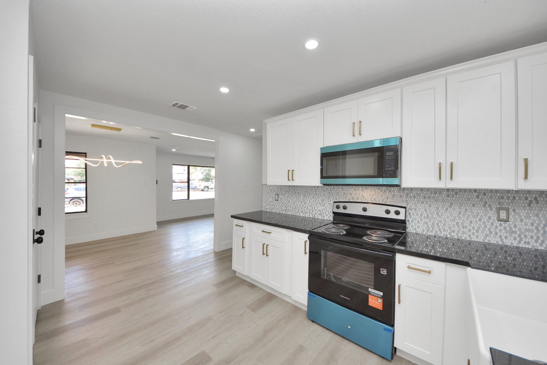 602 Gammon Drive, Houston, TX 77022 Modern kitchen with sleek black countertops, white cabinetry, and stainless steel appliances, seamlessly flowing into a bright, open living area with large windows.