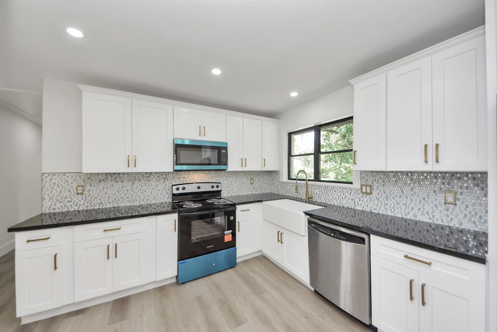 602 Gammon Drive, Houston, TX 77022 Modern kitchen featuring sleek black countertops, white cabinetry, and a stylish mosaic backsplash. Equipped with stainless steel appliances and a farmhouse sink, it offers both functionality and elegance.