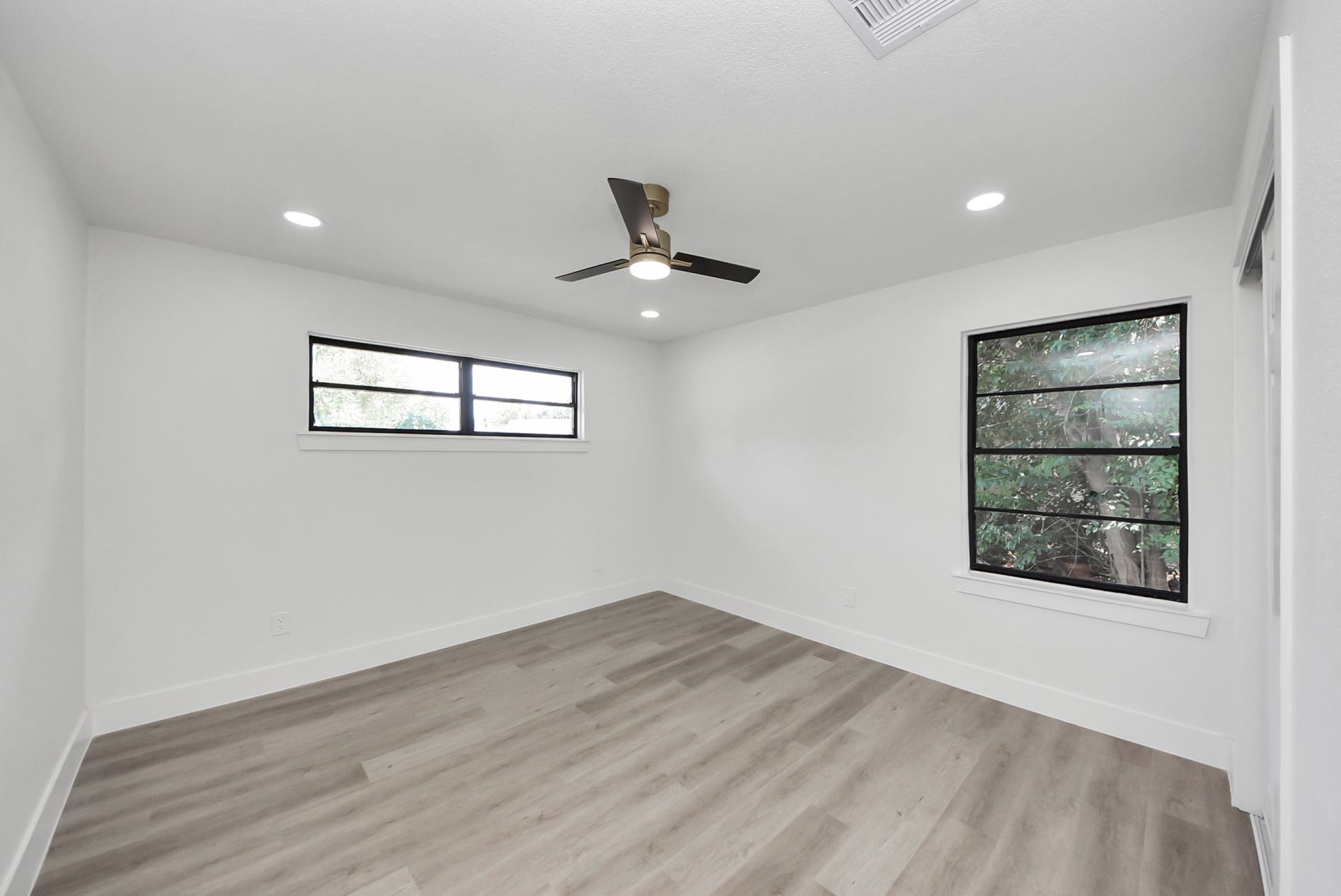 602 Gammon Drive, Houston, TX 77022 Bright, modern room featuring sleek wood flooring, recessed lighting, and large windows with views of lush greenery.