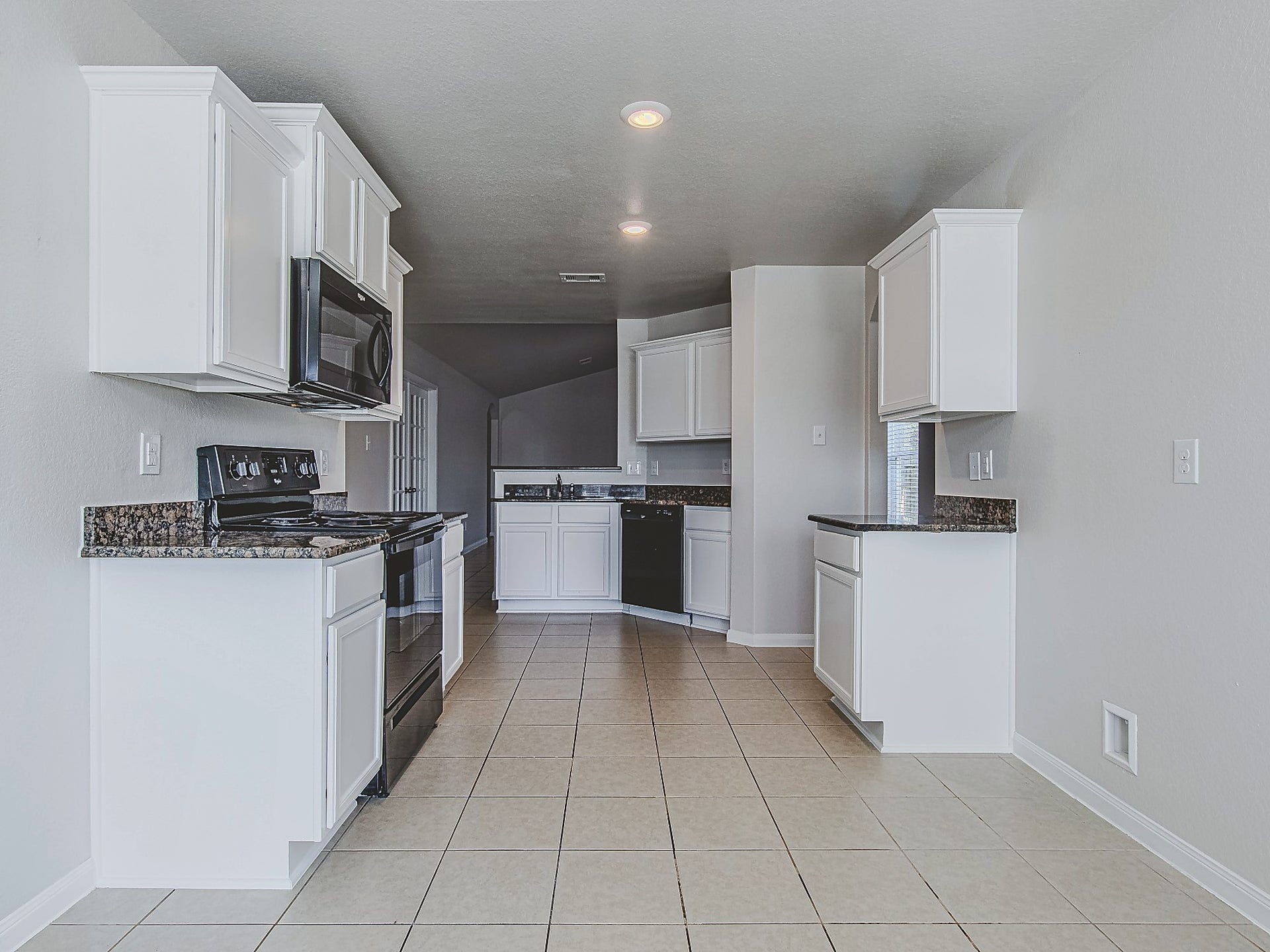 1223 Emerald Stone Drive, Rosharon, TX 77583 This alternate kitchen view showcases the white cabinetry, contrasting granite countertops, and tile flooring carried throughout the space.