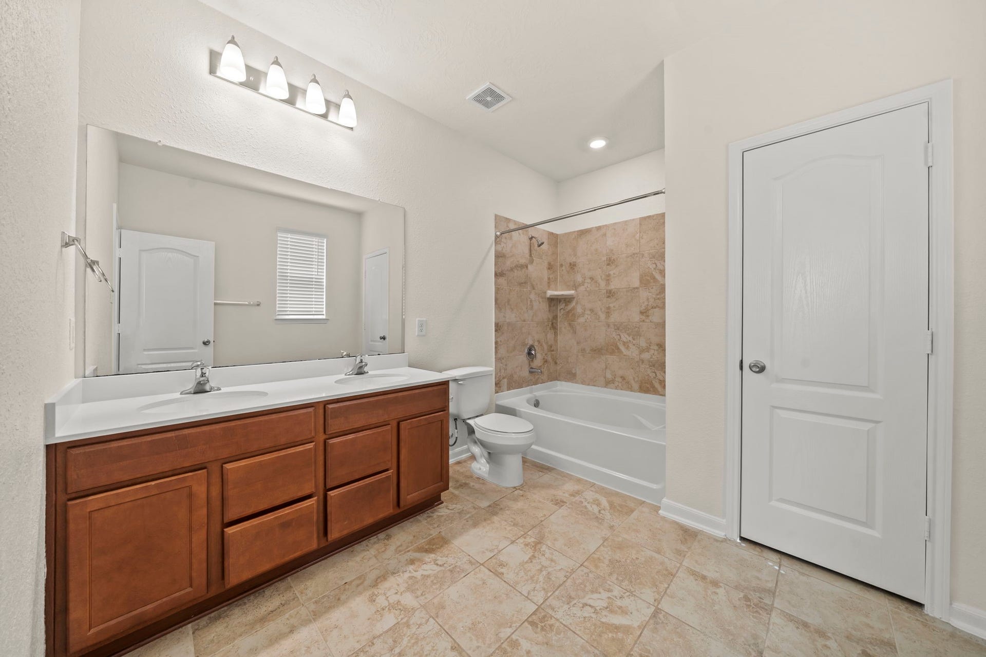 8908 Bear Mountain Court, Magnolia, TX 77354 Spa-inspired primary bath featuring a dual-sink vanity with wood cabinetry, vanity mirror, and neutral tile flooring.