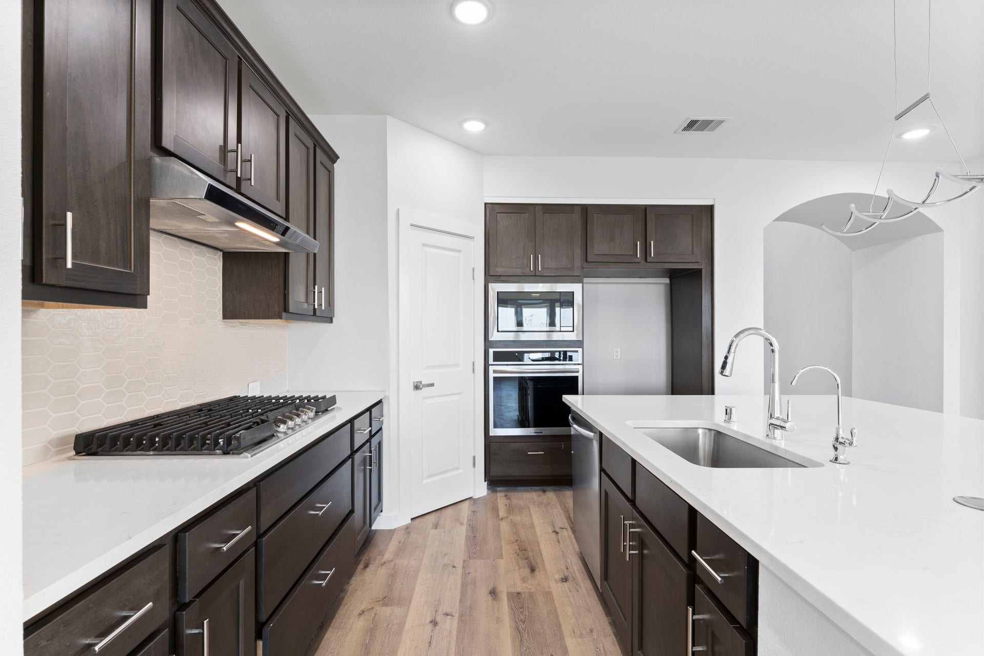 2230 Fresh Flower Way, Richmond, TX 77406 This close-up reveals a premium gas cooktop, sleek stainless steel vent hood, and a modern textured backsplash.