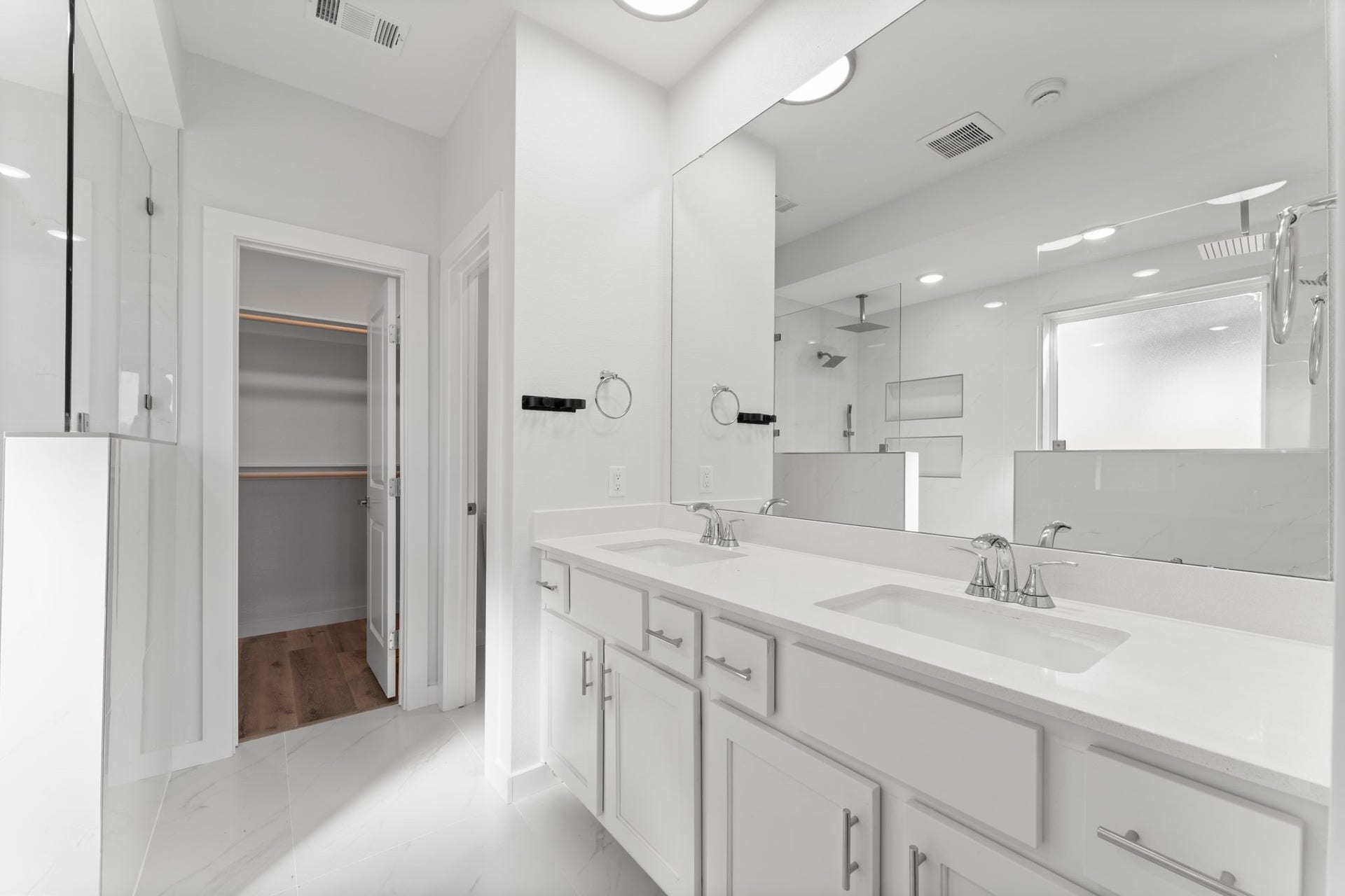 2230 Fresh Flower Way, Richmond, TX 77406 This bright and modern bathroom boasts an expansive double vanity with sleek white cabinetry, quartz-style countertops, and a massive mirror that reflects the room's abundance of light.
