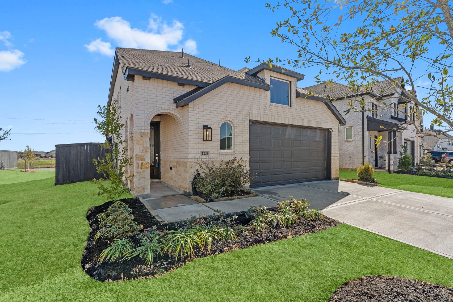 2230 Fresh Flower Way, Richmond, TX 77406 This perspective showcases the beautiful stone accents and the inviting arched entryway. The contrast between the light masonry and dark trim offers a sophisticated, contemporary aesthetic that stands out in the neighborhood.