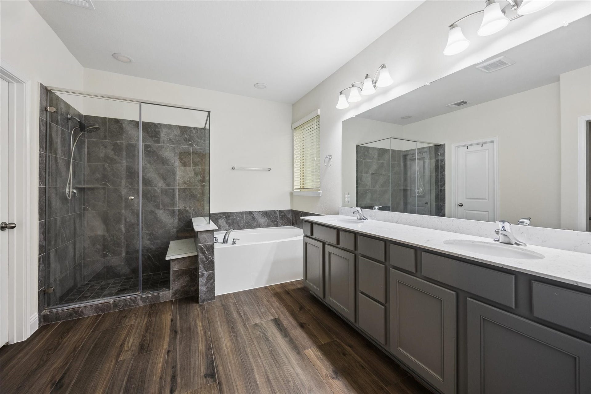 20338 Sienna Bluff Drive, Cypress, TX 77433 Spacious primary bathroom featuring a large dual-sink vanity with ample storage, a deep soaking tub, and a separate glass-enclosed walk-in shower with elegant tile surround. Neutral finishes, a large mirror, and abundant lighting create a bright, polished retreat, complemented by warm wood-look flooring.
