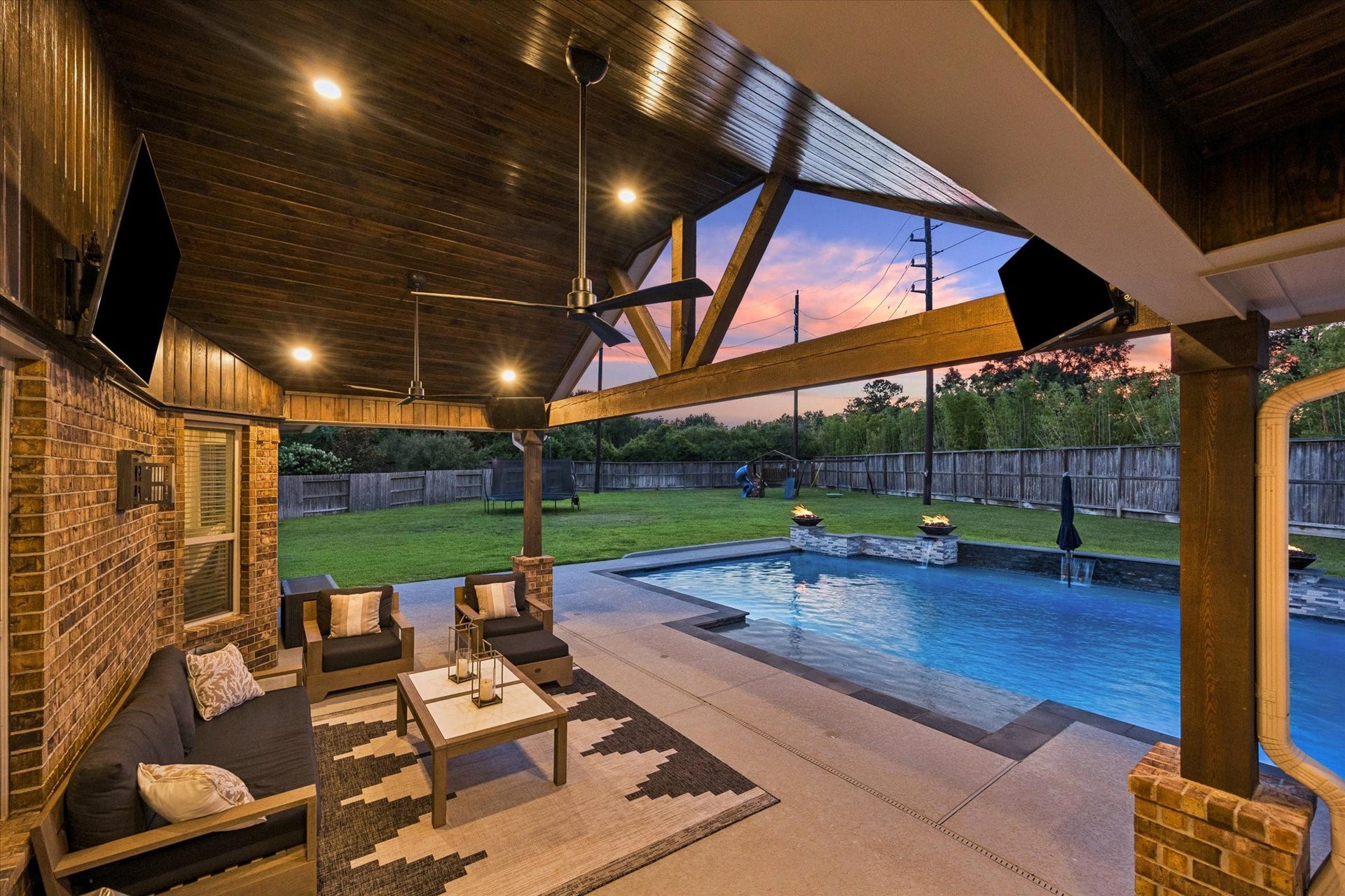 20338 Sienna Bluff Drive, Cypress, TX 77433 Designed for effortless indoor-outdoor living, this spectacular covered patio creates a true private retreat overlooking the resort-style pool. Rich wood-paneled ceilings, exposed beams, and warm recessed lighting bring a sophisticated lodge-inspired character to the space, while comfortable lounge seating provides the perfect setting for relaxing or entertaining.