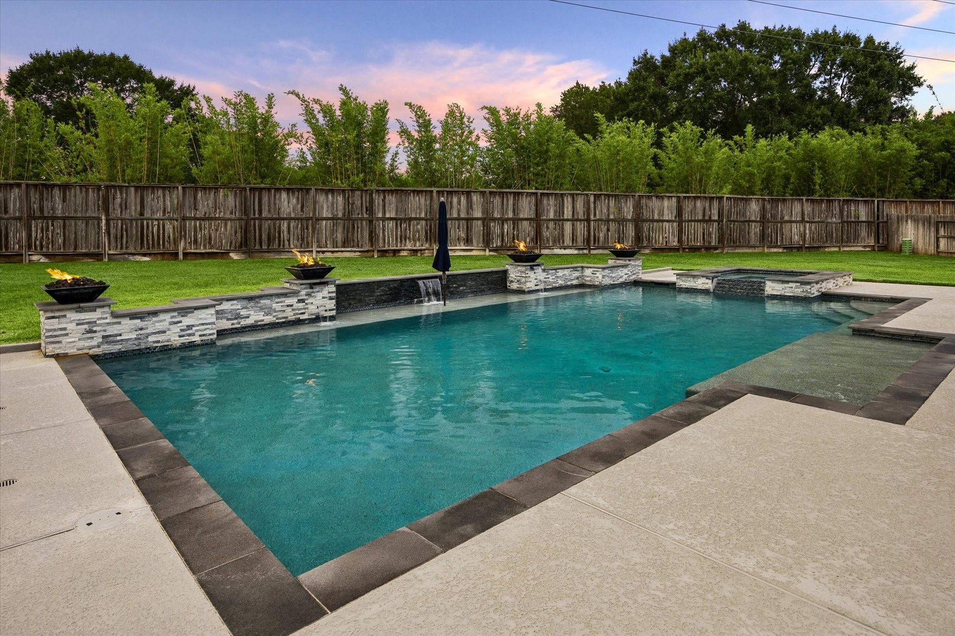 20338 Sienna Bluff Drive, Cypress, TX 77433 This expansive sparkling pool, framed by elegant stone accents, cascading water features, and dramatic fire bowls that create a stunning ambiance from day into evening. The generous pool deck provides plenty of room for lounging and entertaining, while the lush, fully fenced yard and mature greenery create a peaceful sense of privacy.