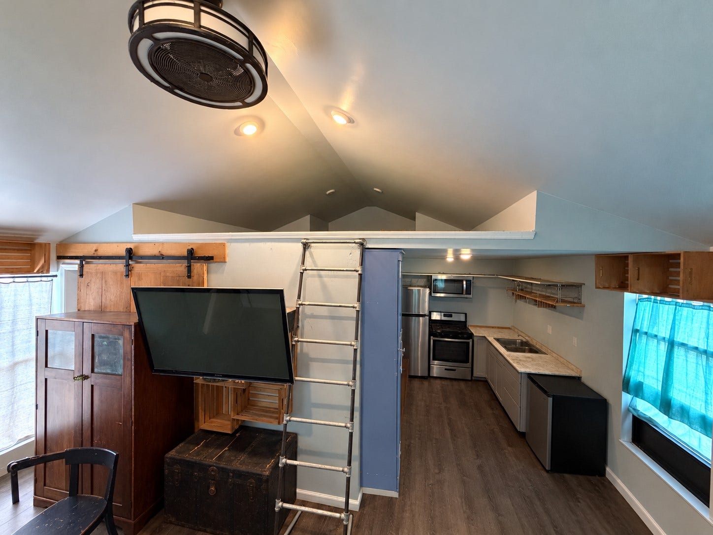 Main living space with vaulted ceilings, ceiling fan, and ladder access to the loft.