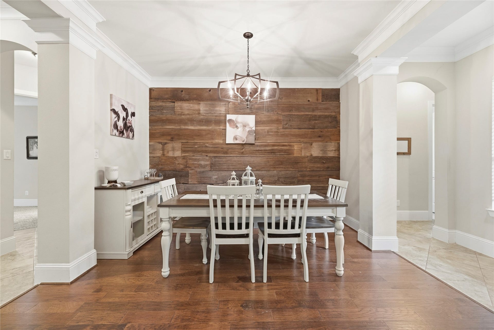 5414 Lake Hill Farm Way, Fulshear, TX 77441 Centered view of the formal dining space showcasing the feature reclaimed-wood accent wall, hanging light chandelier, crown molding, dark wood-look floor, and architectural side columns separating the room from adjacent halls.